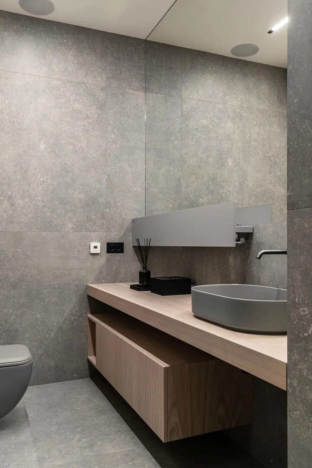 A modern minimalist bathroom featuring concrete tiles and a contemporary vanity with a wood finish.