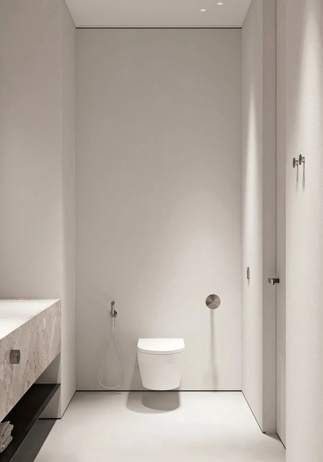 A minimalist white bathroom with a toilet and hand shower.