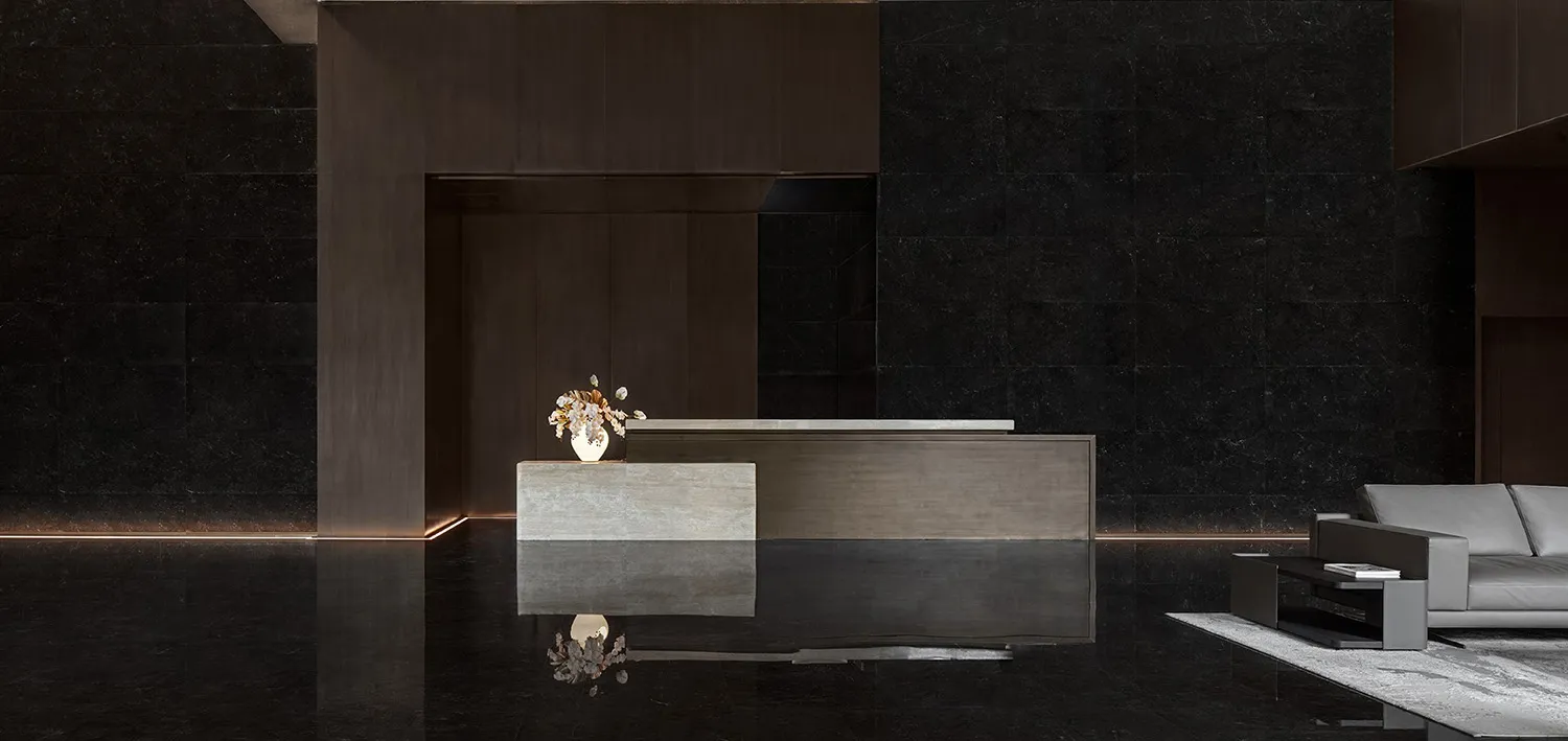 A modern lobby with a concrete reception desk, white vase with flowers, and a grey sofa on a white rug.