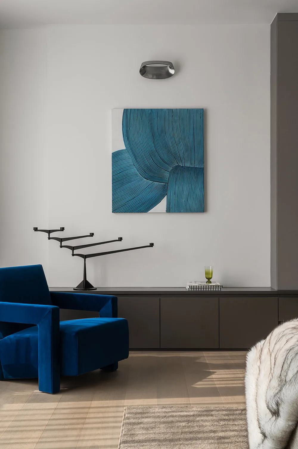 Modern living room featuring a blue velvet couch, abstract art, and sleek, dark wooden cabinets.