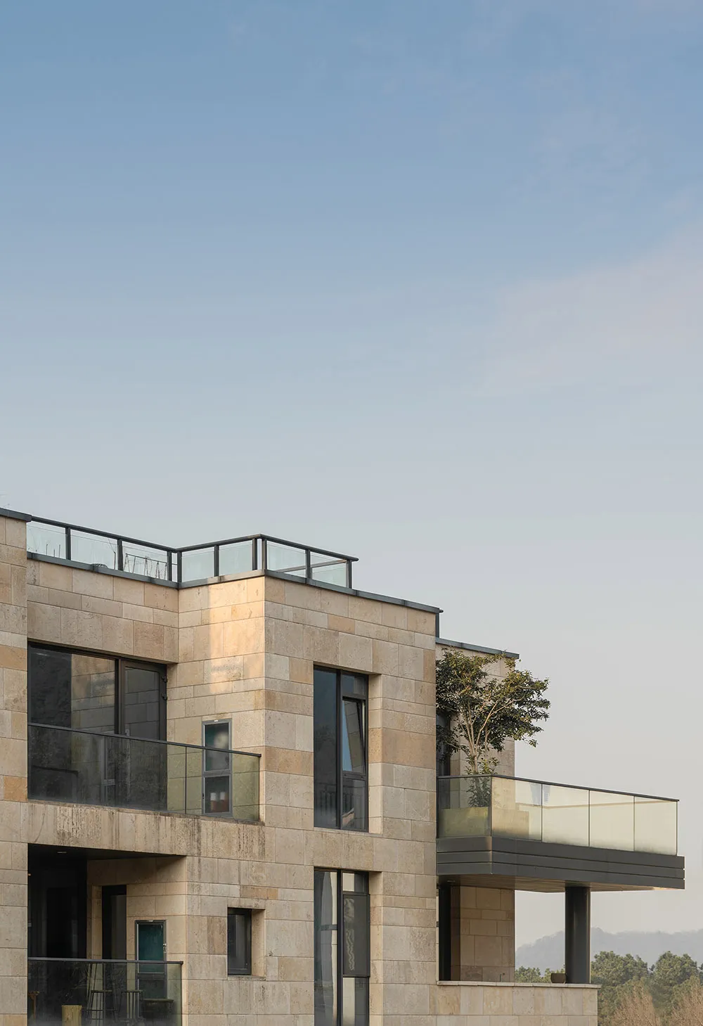 Modern, minimalist residential building with stone exterior, glass windows, and rooftop balcony.