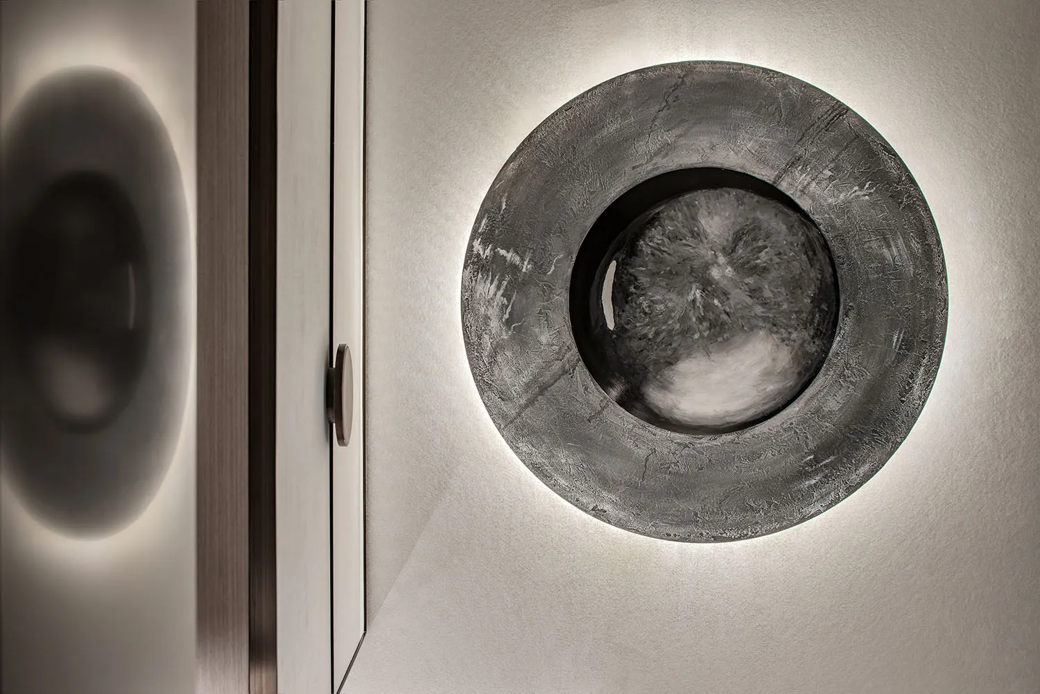 A modern interior design featuring a round, textured concrete lighting fixture mounted on a white wall.