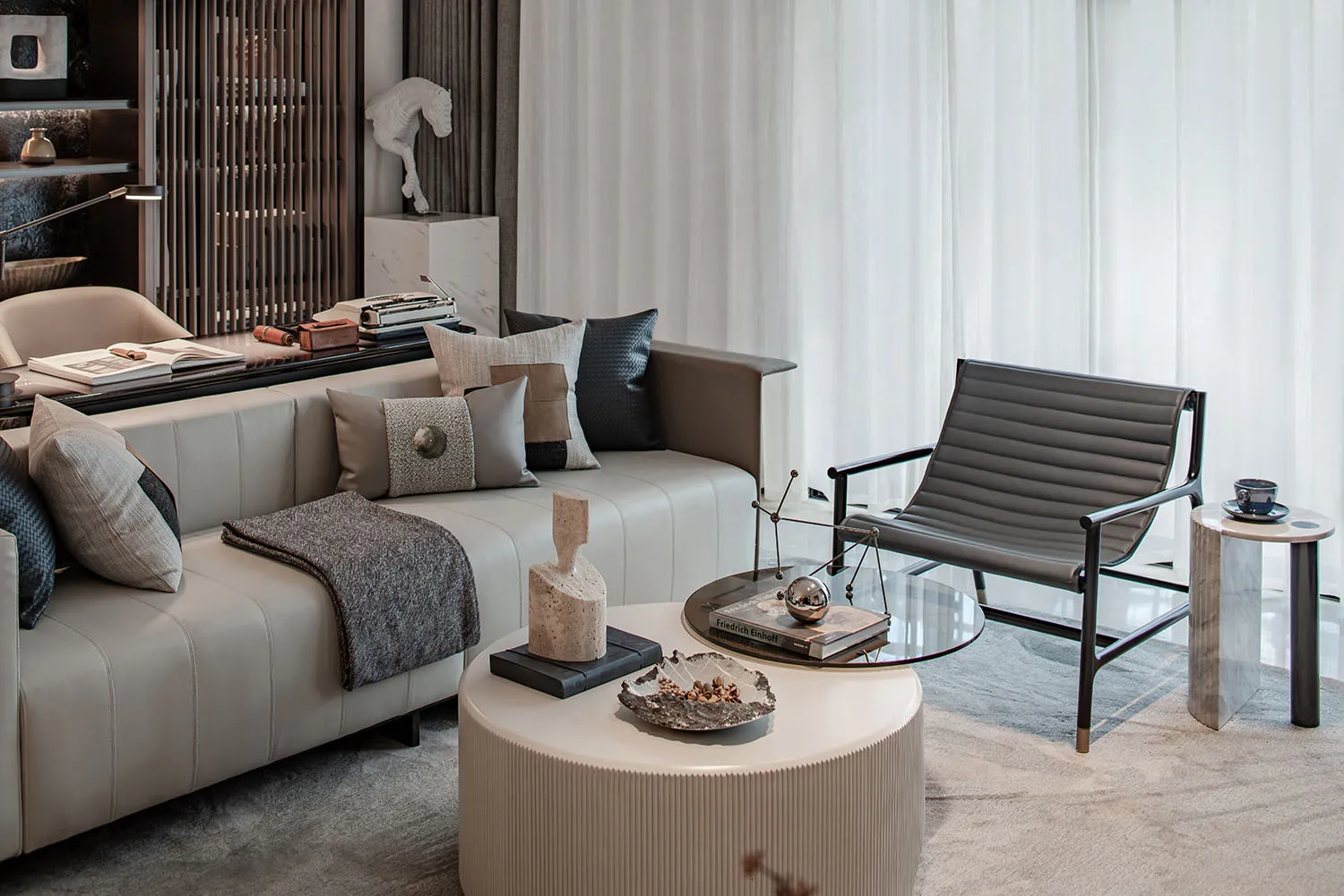 A modern living room with neutral-toned furniture, including a white sofa with patterned pillows, a glass coffee table, and a