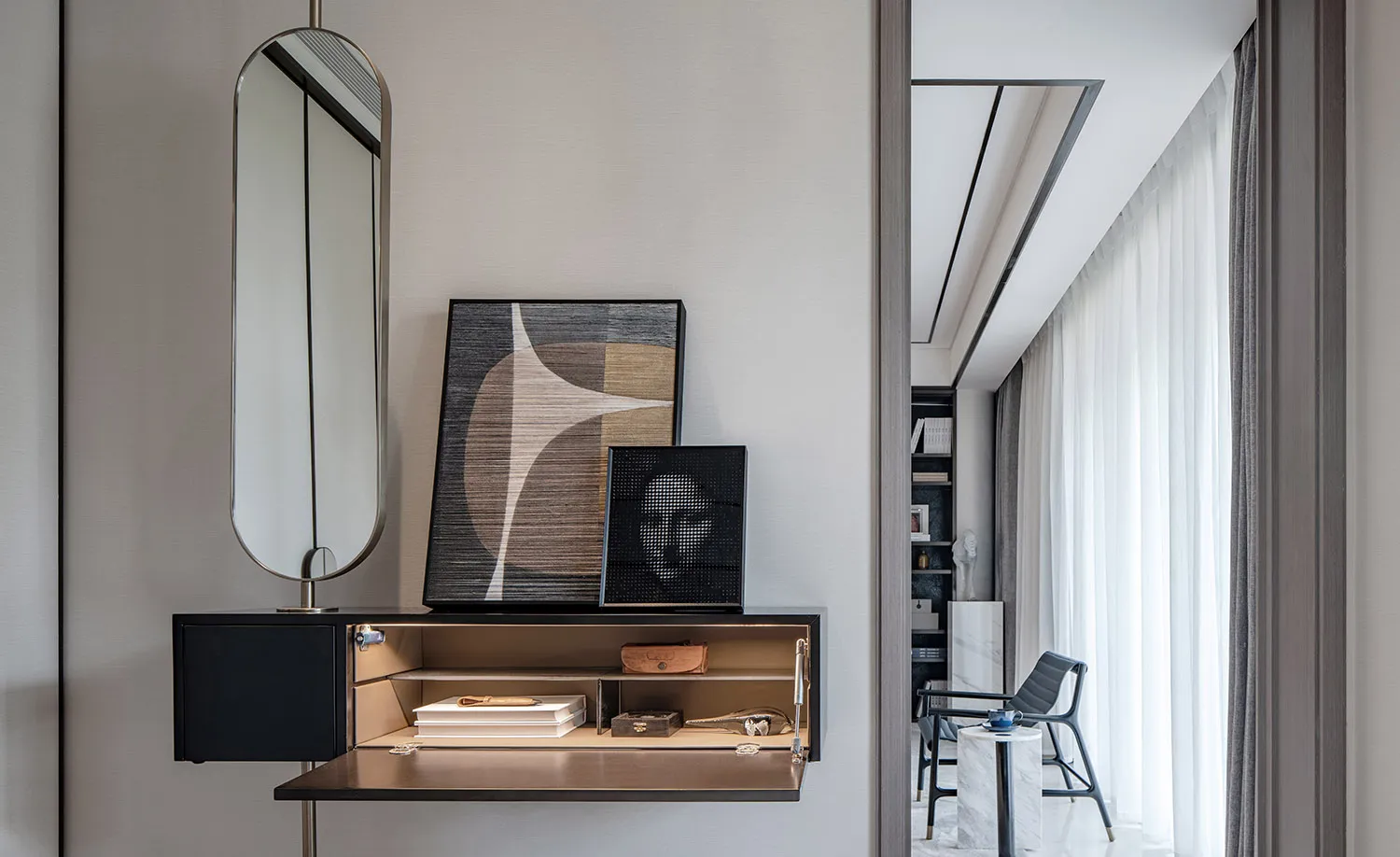 A modern living room with a desk featuring a sleek, black shelf and storage compartments, topped with abstract art pieces and