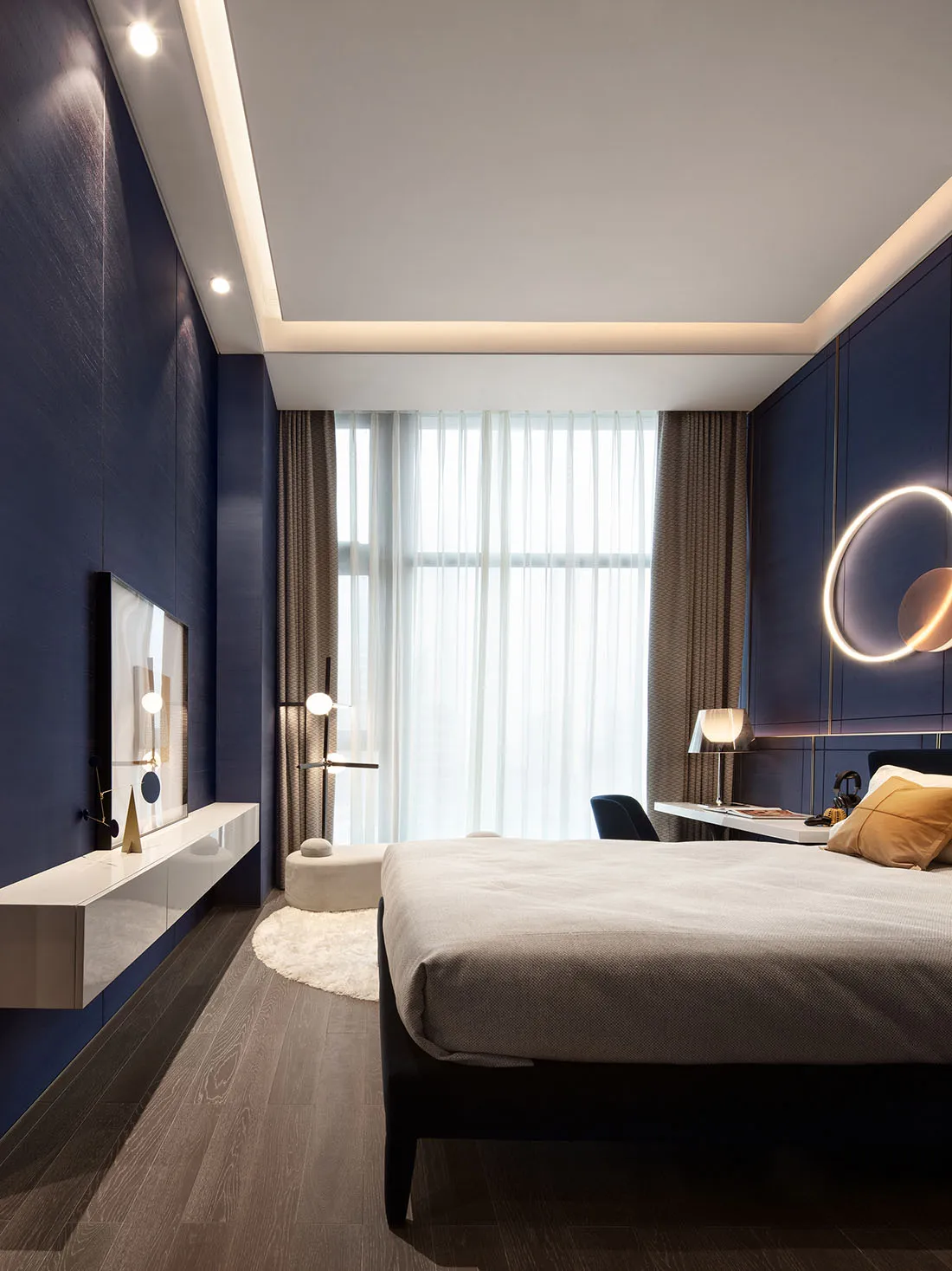 Minimalist bedroom with dark blue walls, textured paper window shades, and a light-colored bed.