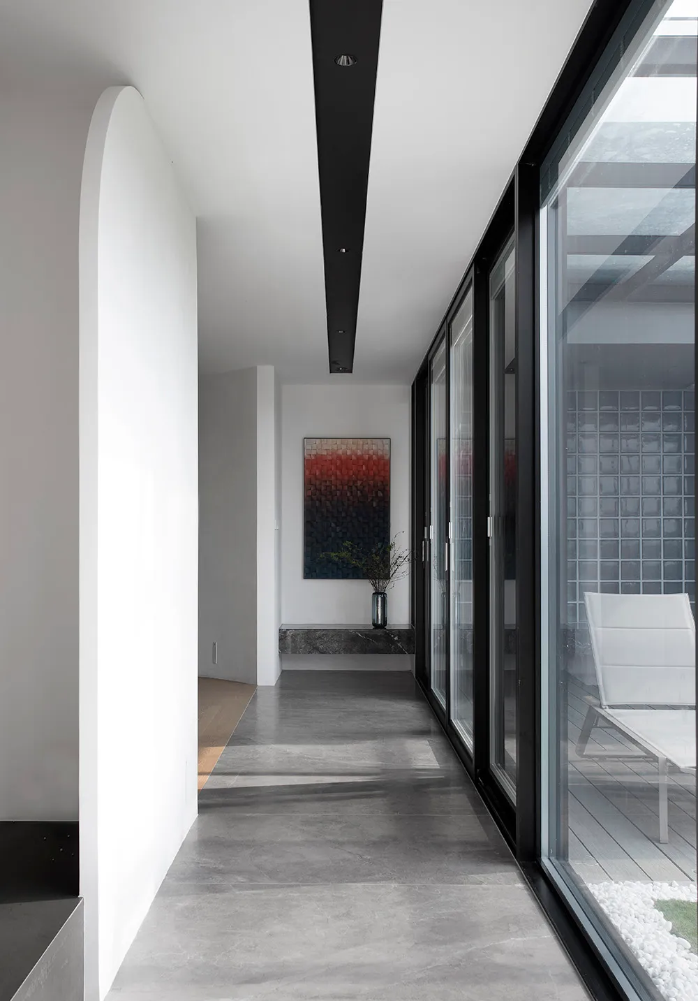 A minimalist interior design featuring a concrete pathway with a view of an outdoor seating area.