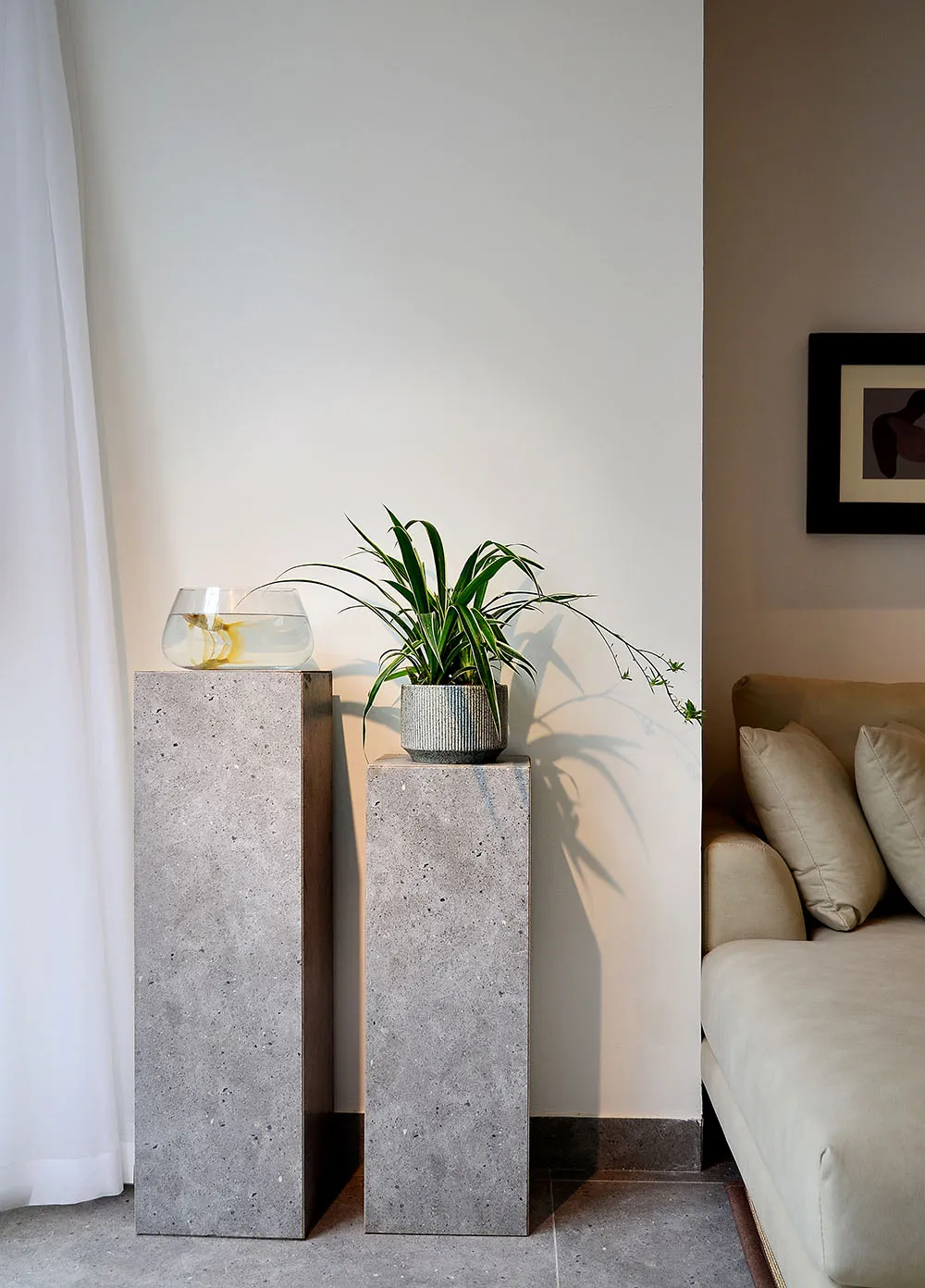 A modern living room with concrete pedestals, houseplants, and a neutral couch.