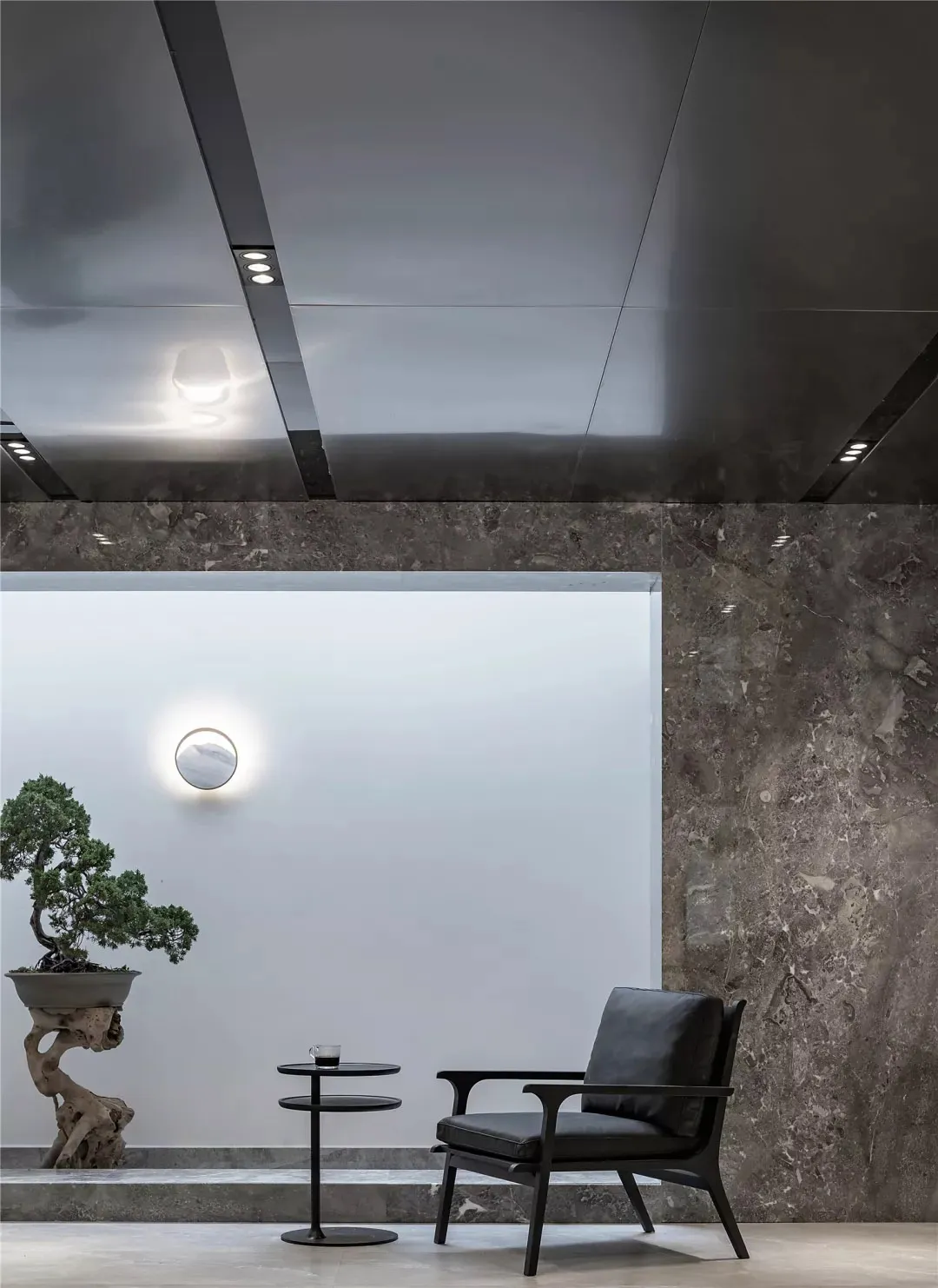 Modern living room featuring a black leather armchair, metallic black coffee table, and marble wall backdrops.