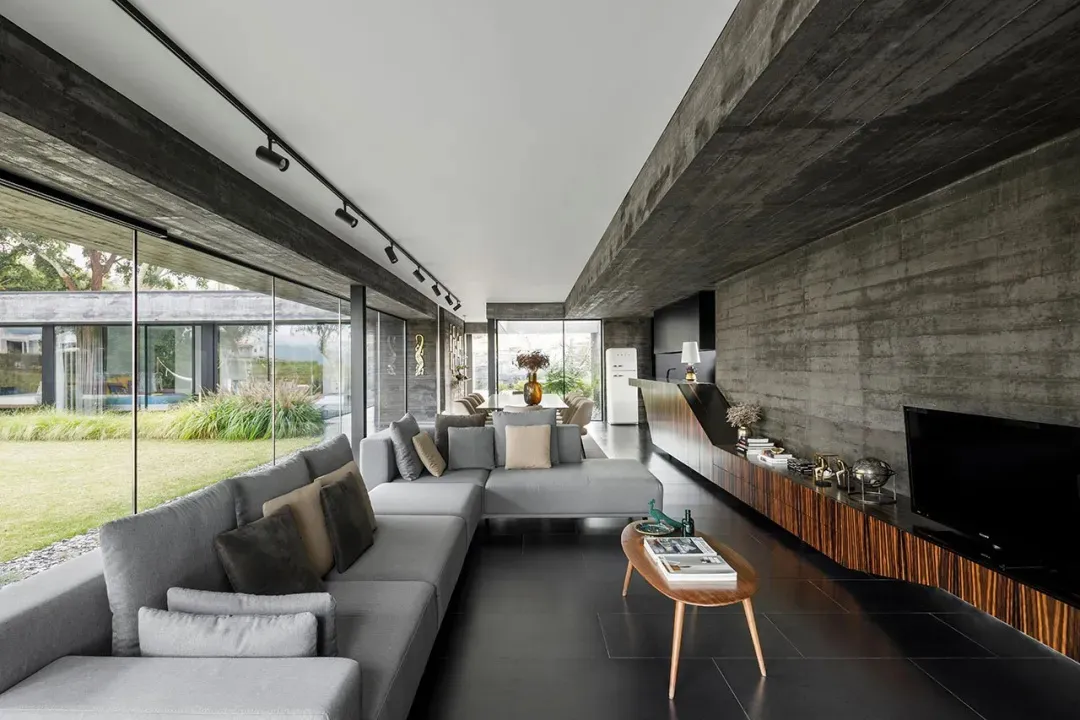 A modern living room with concrete walls, large windows, and a comfortable sectional sofa.