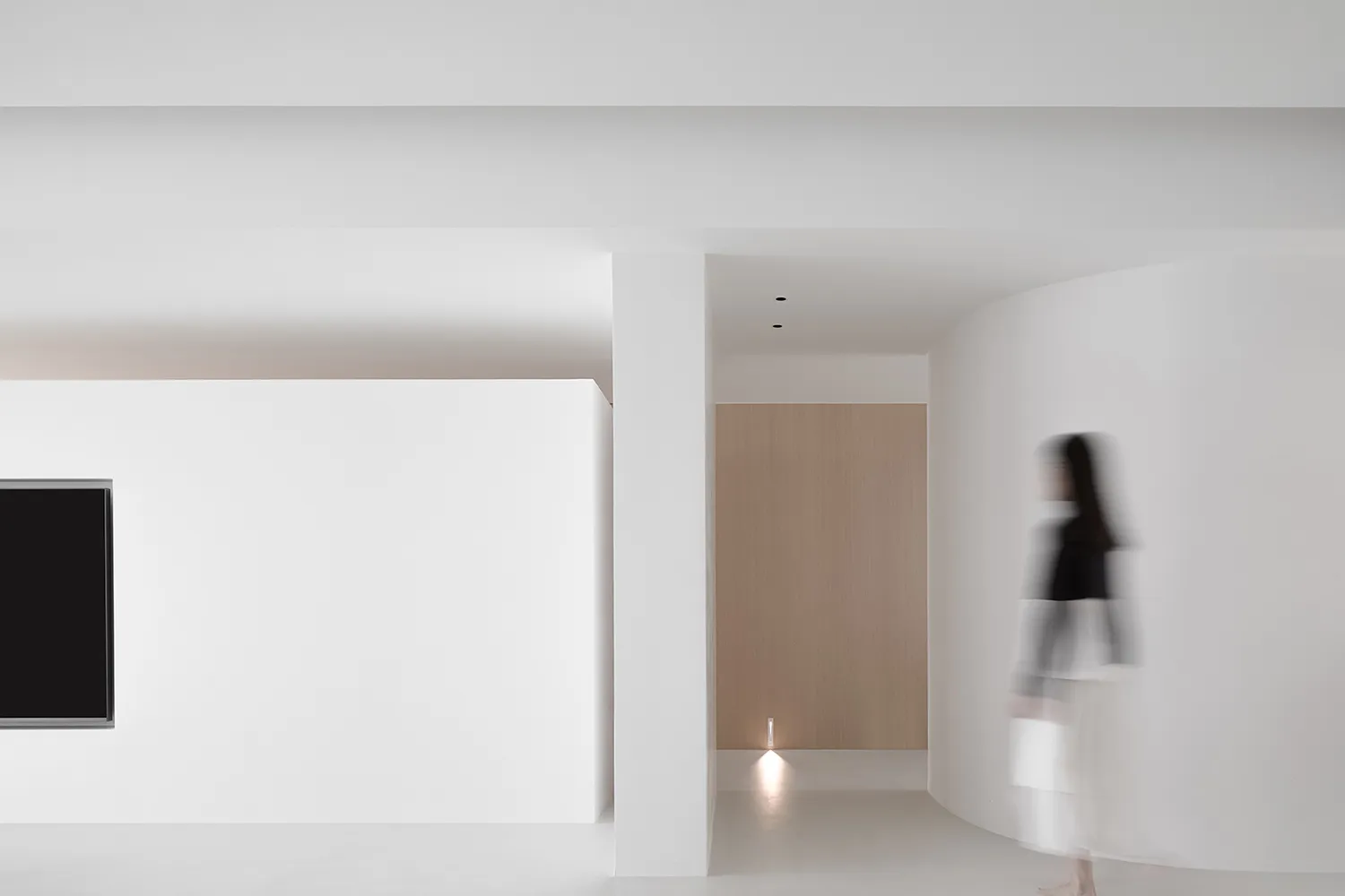 A minimalist white corridor with soft lighting and a person blurred in motion.