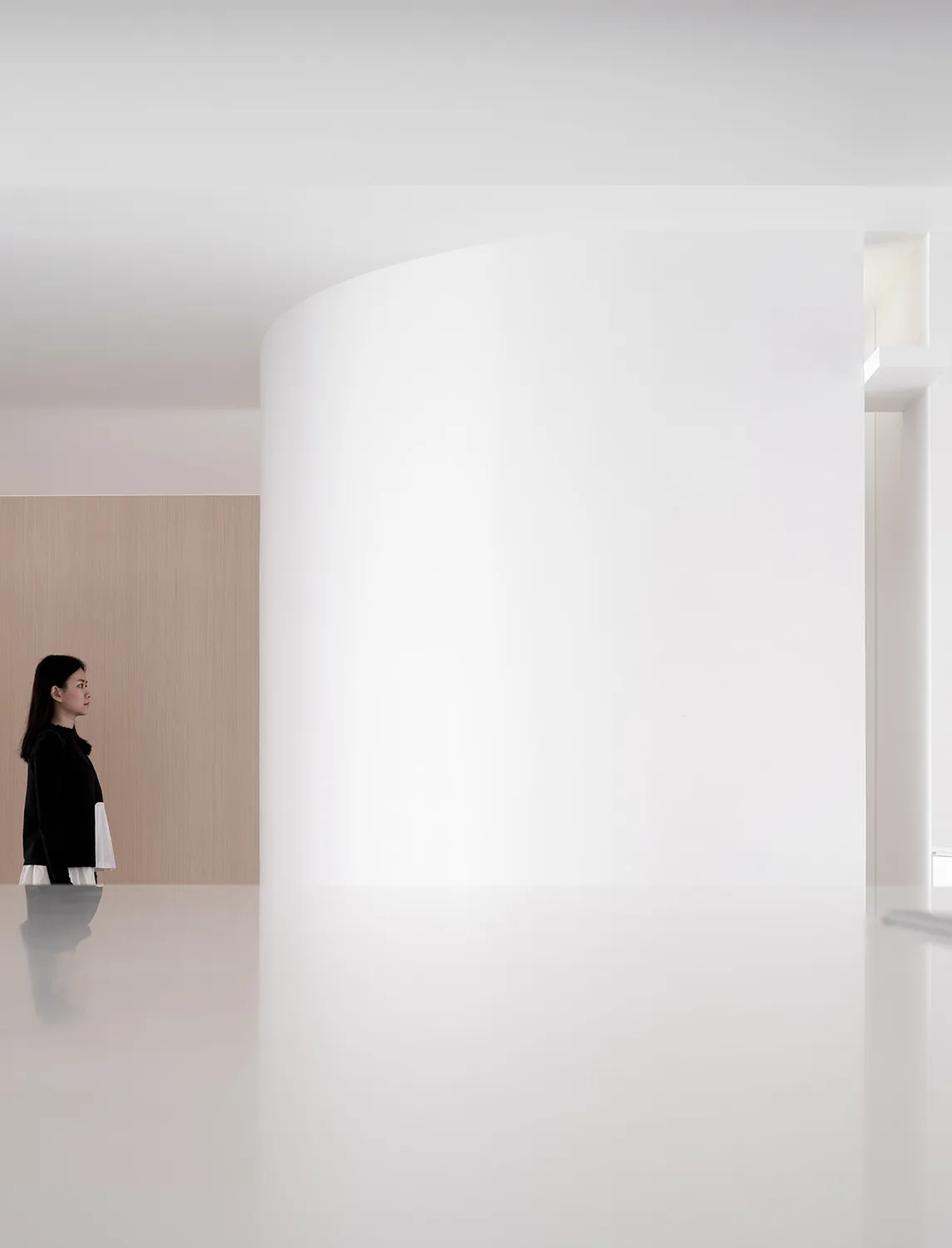 A minimalist white interior space featuring a curved white wall and a person standing in the foreground.