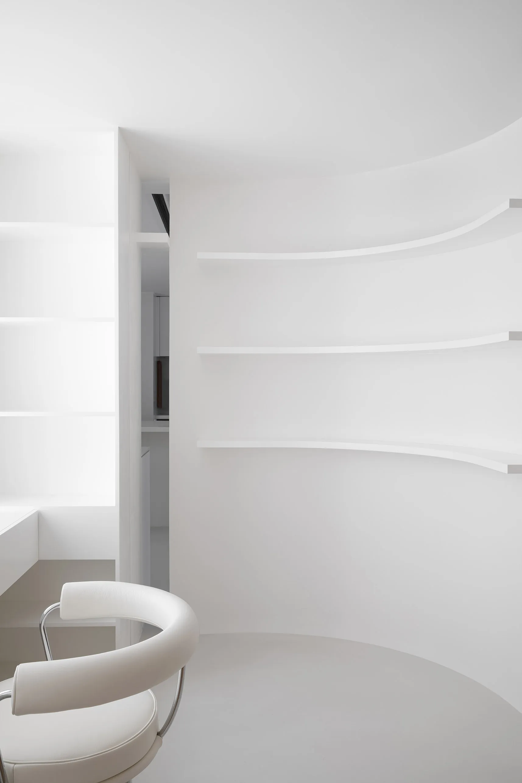 A minimalist white interior design space featuring a circular table and a white chair.