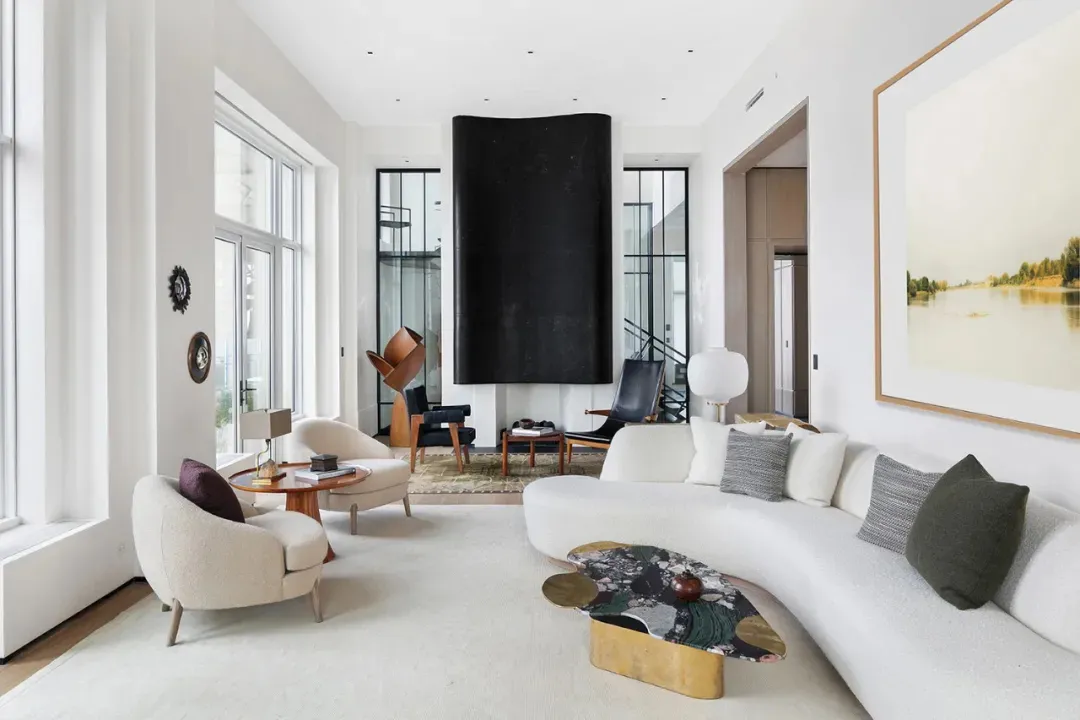 A minimalist living room with a sleek, white curved sofa, a patterned coffee table, and a large window.