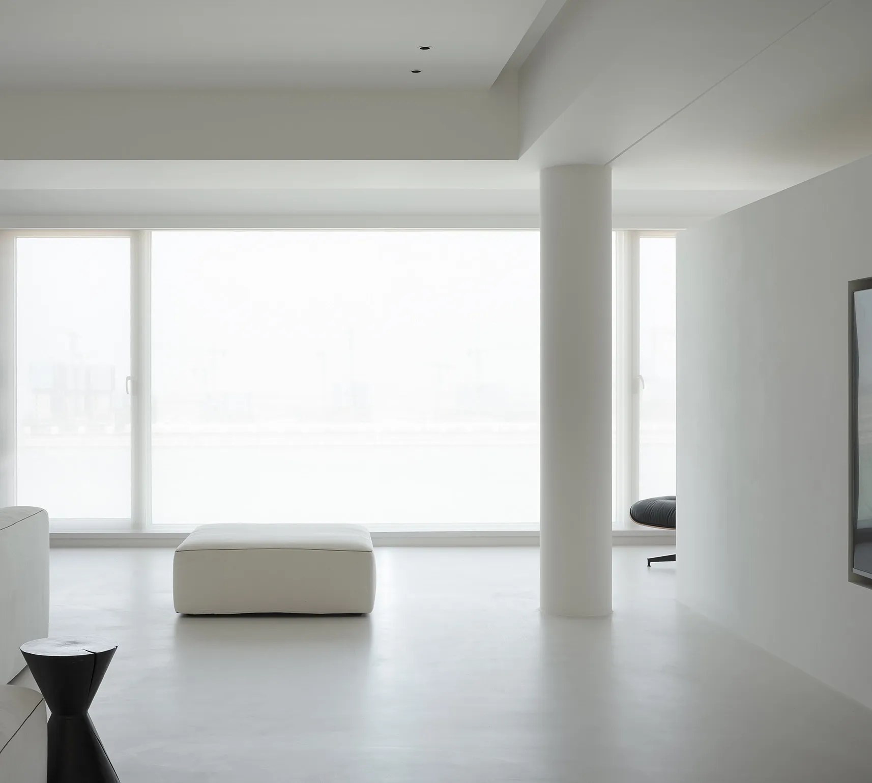 A minimalist living room with white concrete flooring and furniture.