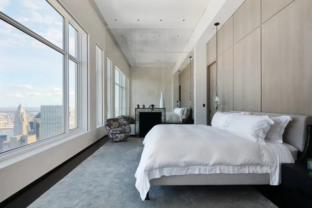 Modern minimalist bedroom with a large window, white bedding, and a floral armchair.