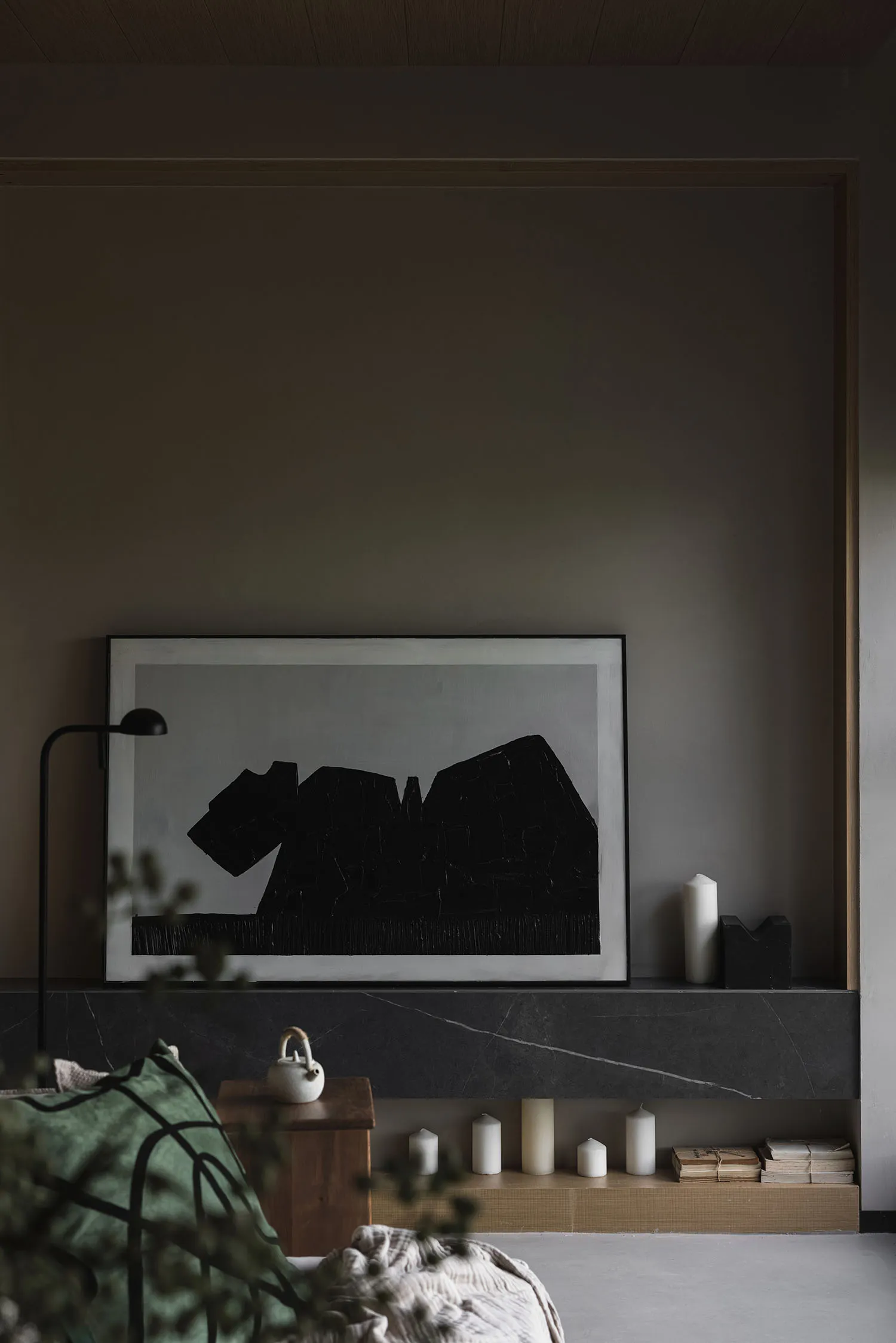 A modern living room with a large black and white abstract artwork, marble fireplace surround, and green throw blanket.