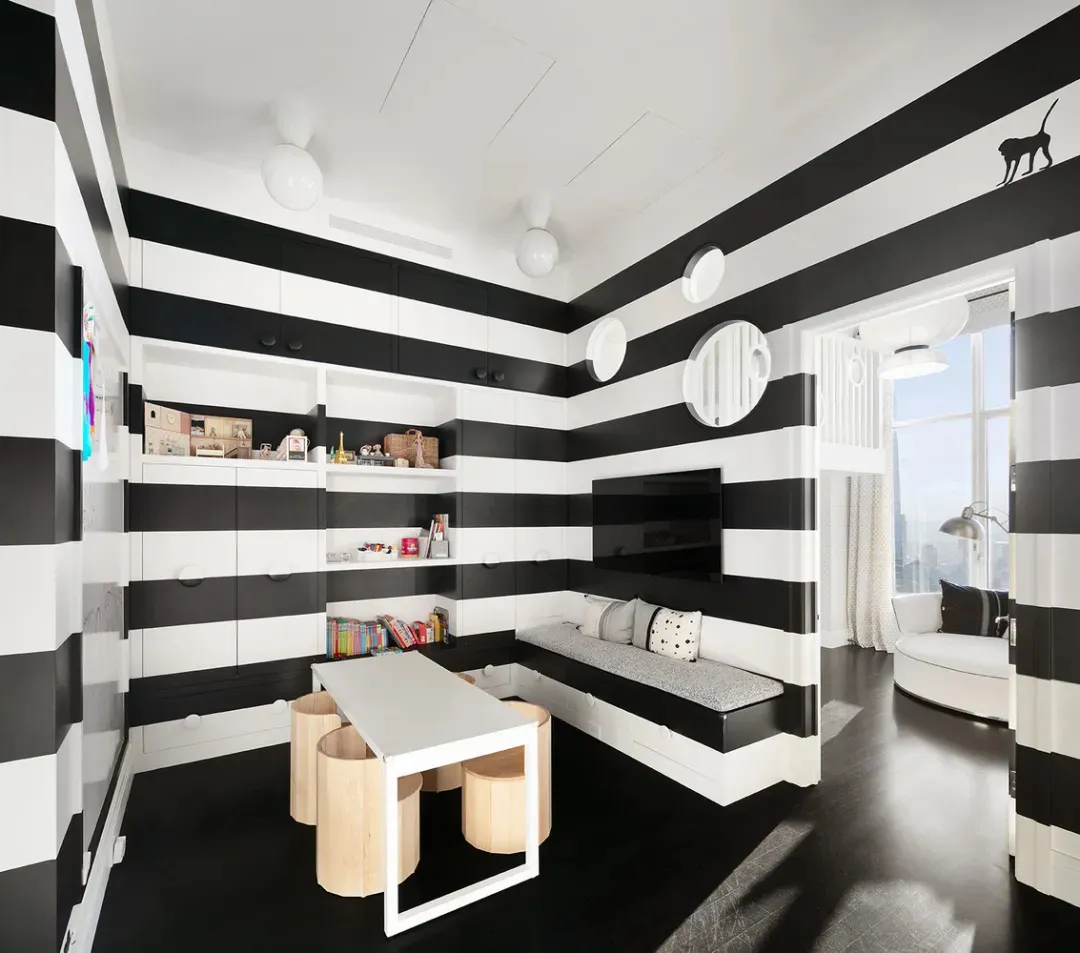 A modern minimalist child playroom featuring black and white striped walls, a built-in seating area, and a table with stools.