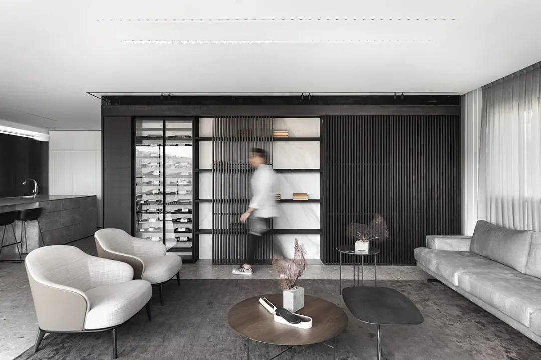 A modern minimalist living room with white furniture, dark wood paneling, and marble accents.