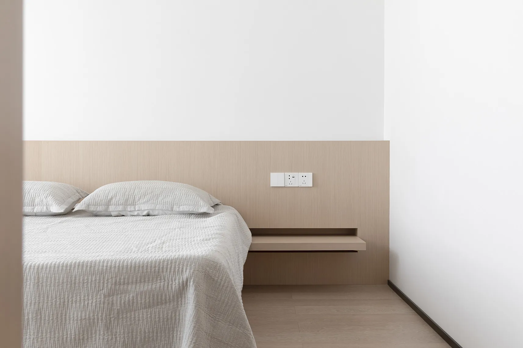 A minimalist bedroom with a white bed on hardwood floors, minimalist wooden headboard and floating nightstand.
