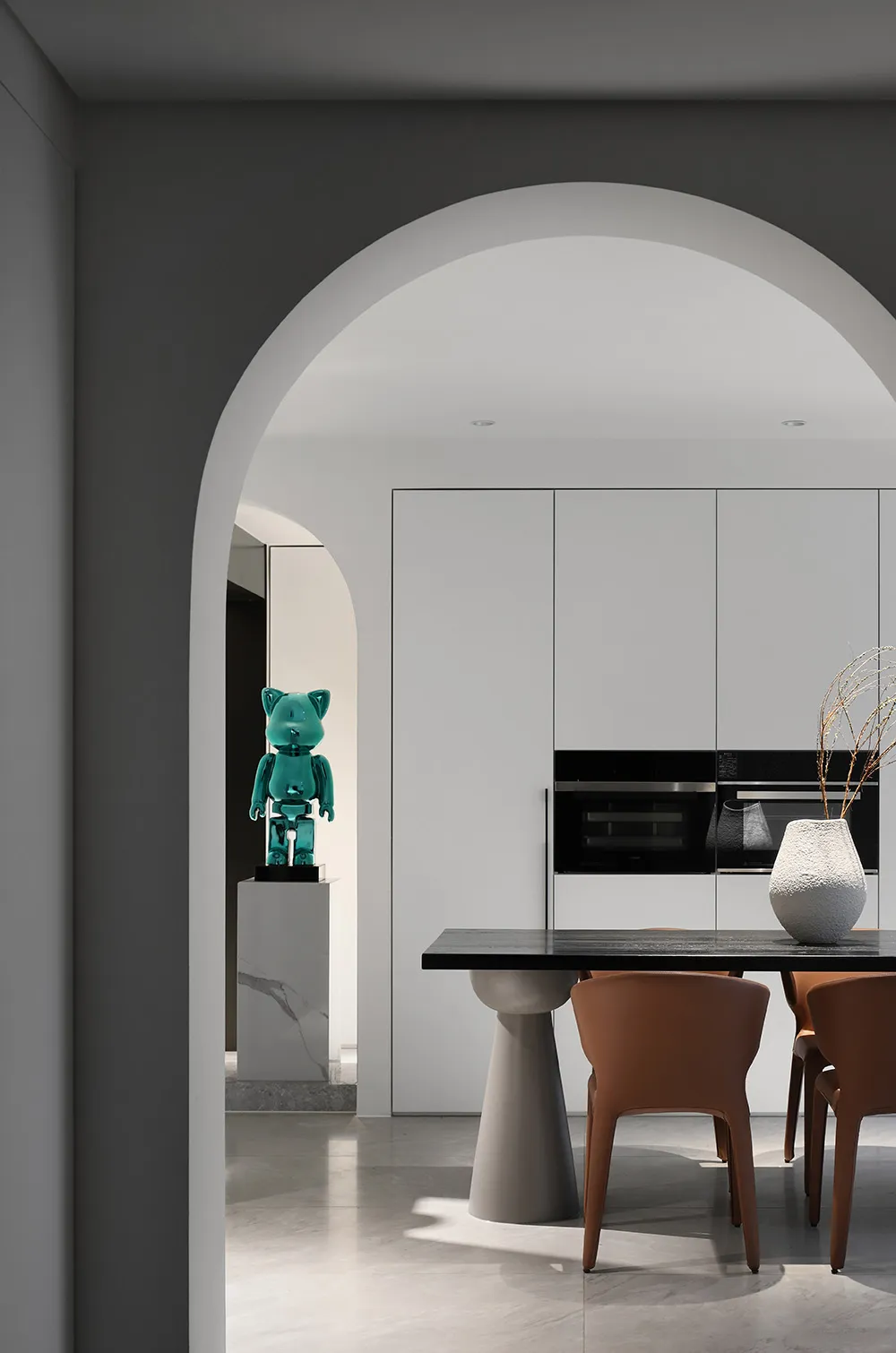 Modern kitchen featuring sleek white cabinets, black countertops, and a shiny green glass sculpture on a pedestal.