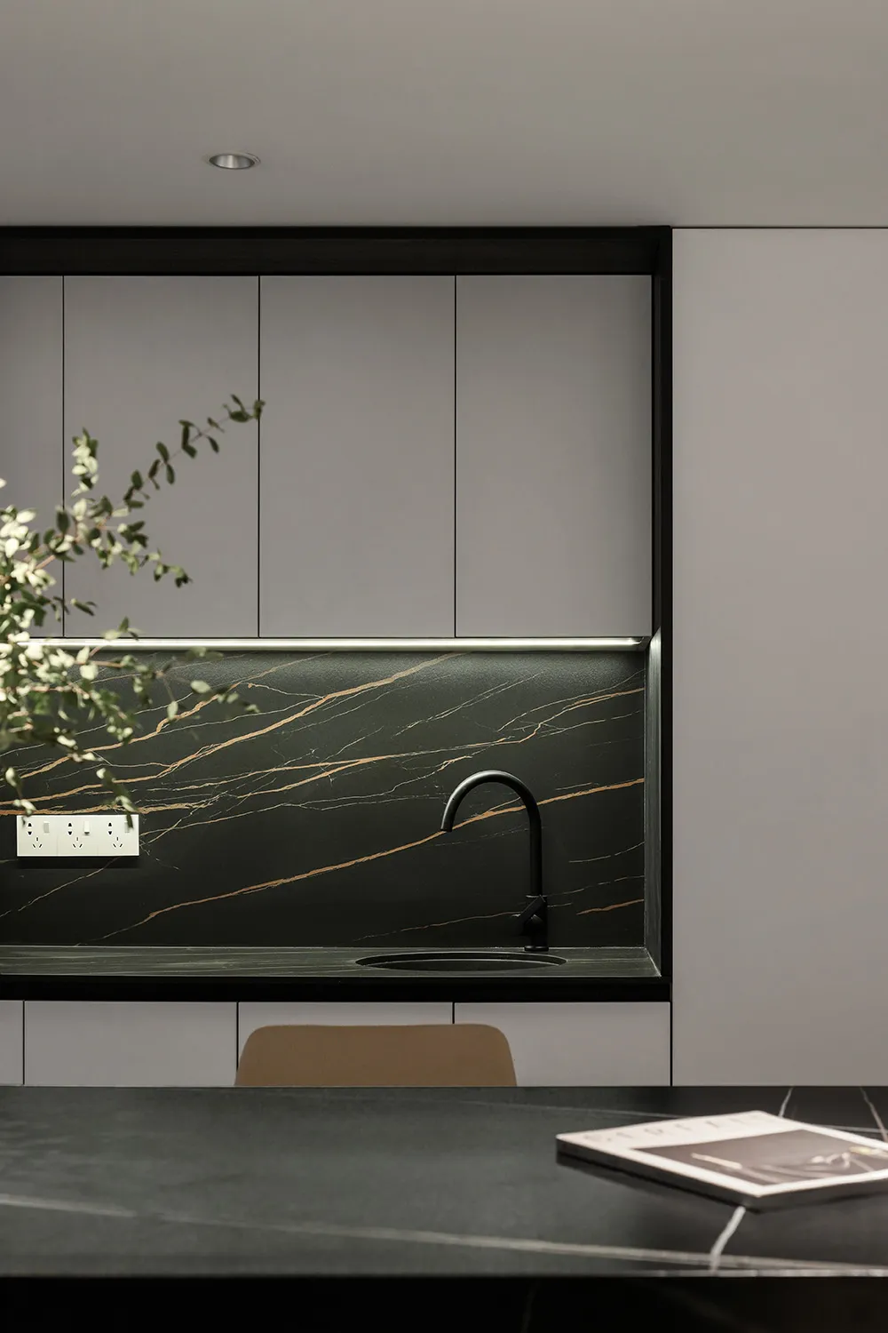 A modern minimalist kitchen features a marble backsplash and countertop with a black faucet and a plant.