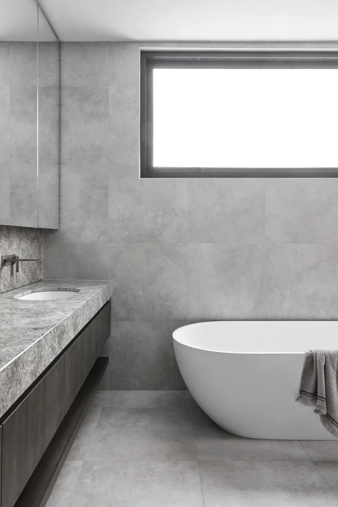 Modern minimalist bathroom with concrete walls, a white freestanding bathtub, and a floating vanity.