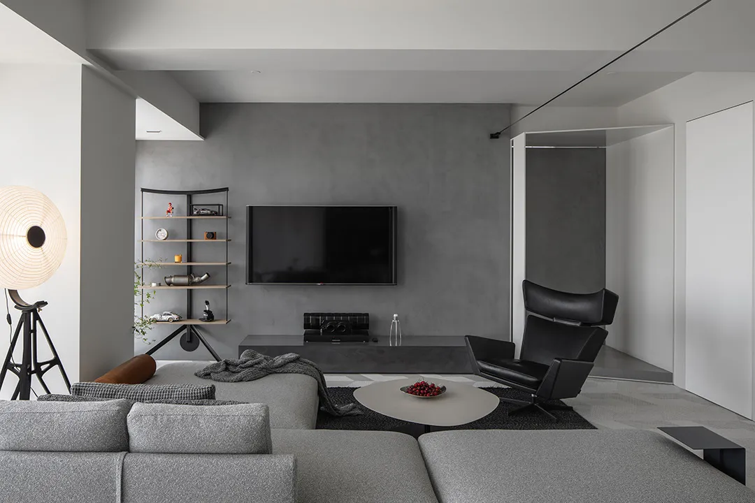 Modern minimalist living room with concrete walls, furniture, and floor, featuring a grey sectional sofa, a round coffee tabl