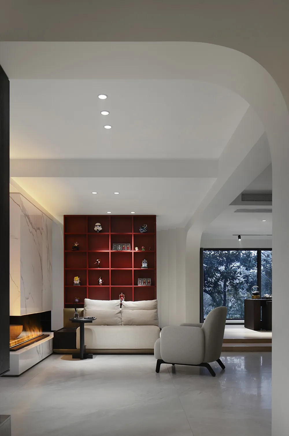 Modern minimalist living room with white walls, wooden floor, red bookshelf, and white furniture.