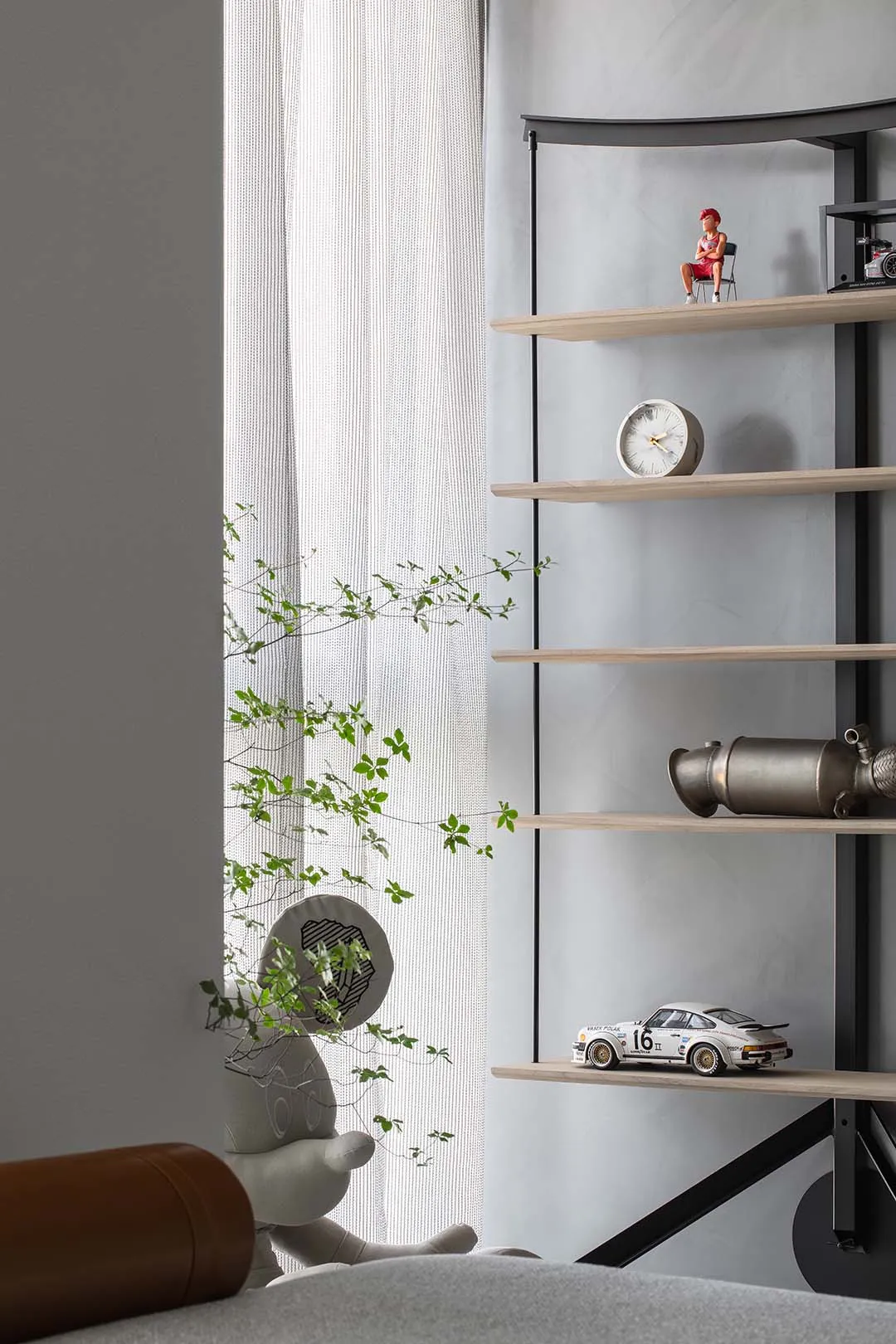 A minimalist shelf decorated with a small figurine, a round clock, a white toy car, and a metallic object.