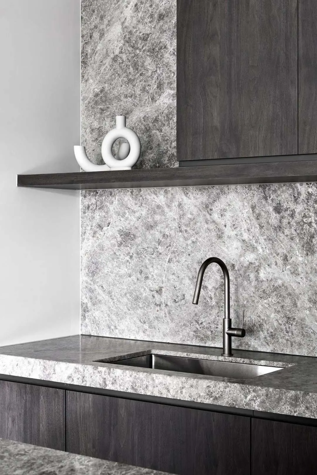 Contemporary kitchen featuring a sleek, minimalist design with dark wood cabinetry and a marble countertop and backsplash.