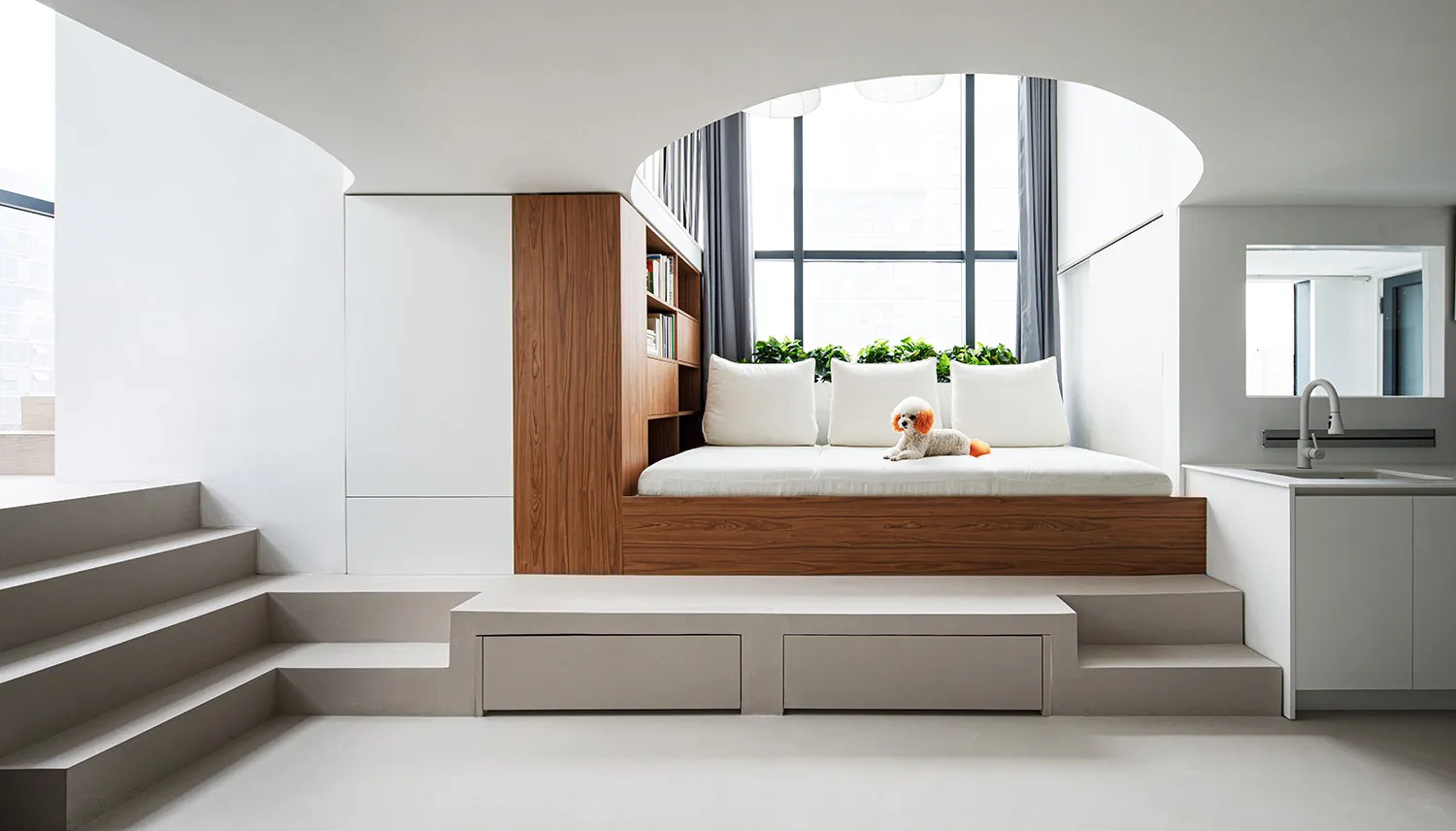 A modern minimalist bedroom with a white bed, wooden headboard, and concrete floor.