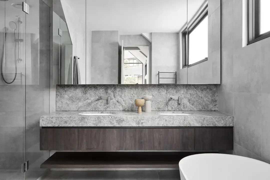 Modern residential bathroom featuring marble countertops and a glass-enclosed shower.