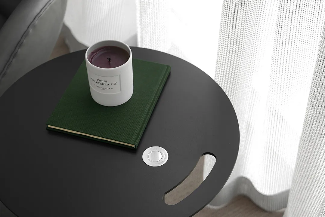 A modern side table with a white ceramic candle holder, a green hardcover book, and a white textured curtain in the backgroun