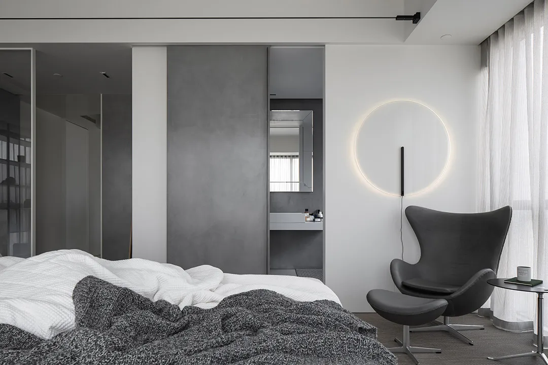 A minimalist bedroom featuring a concrete wall and a circular light fixture.