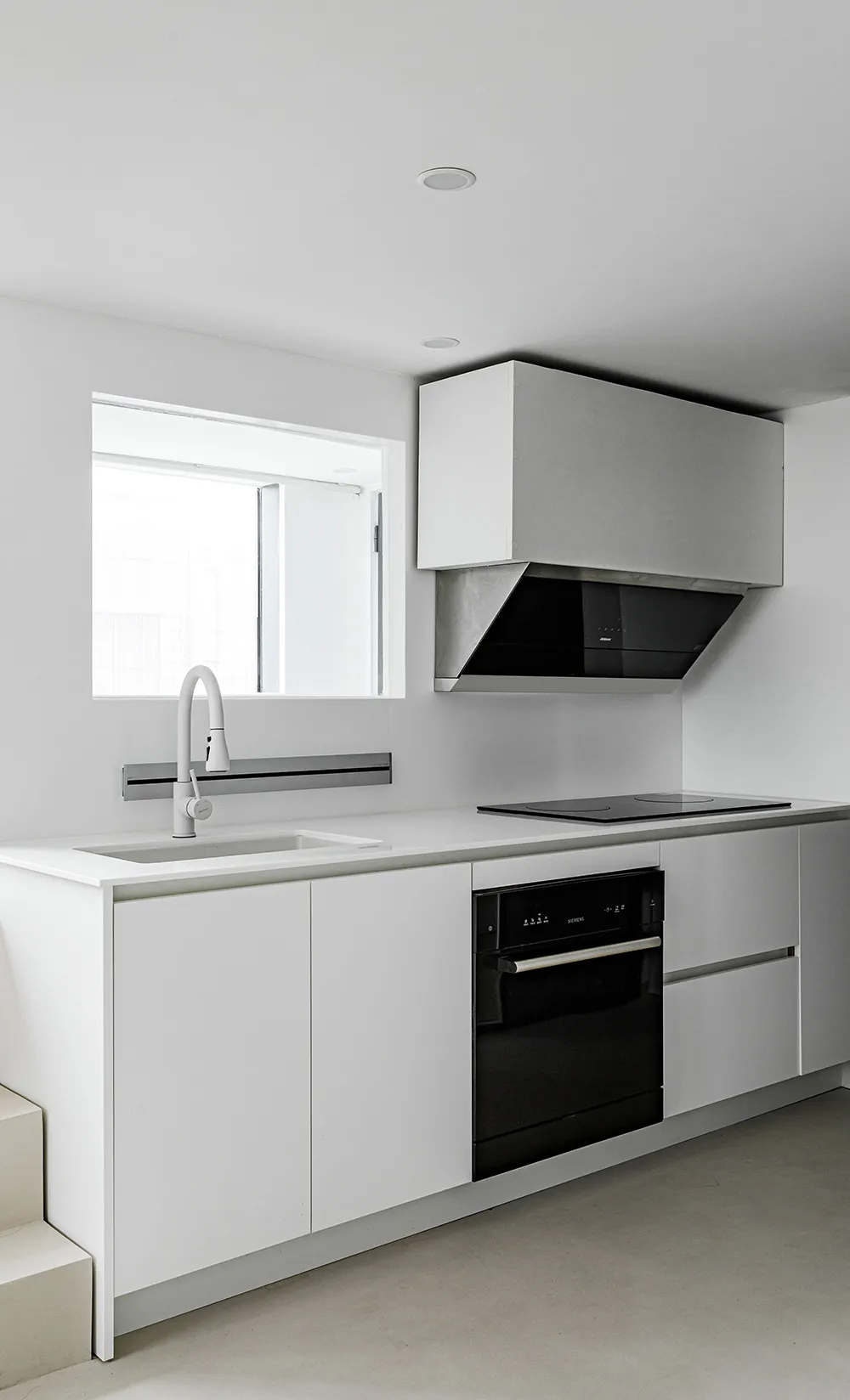 Modern minimalist kitchen with white cabinets, stainless steel appliances, and a white sink.