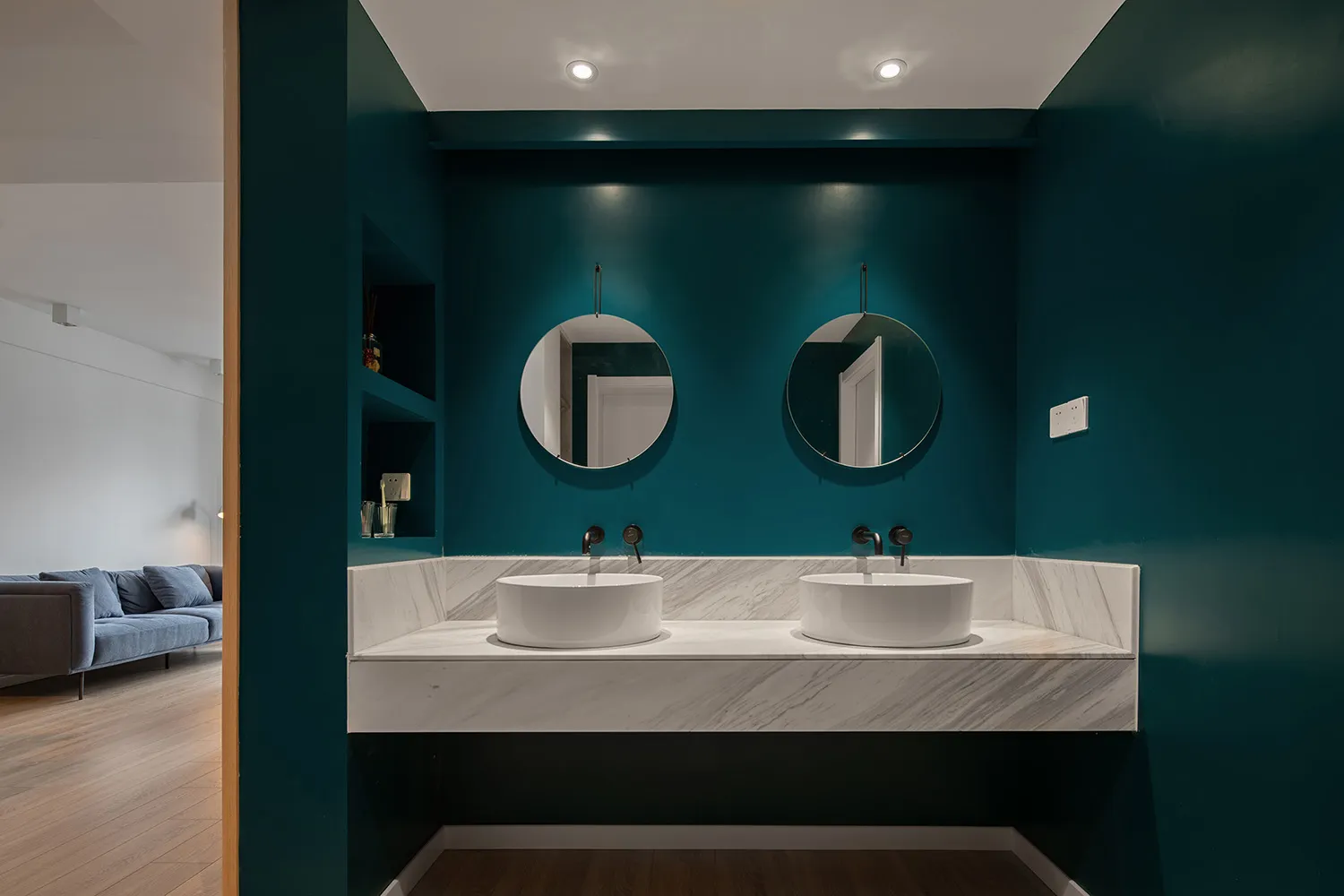 Modern bathroom with marble cladding, white sinks, and circular mirrors.