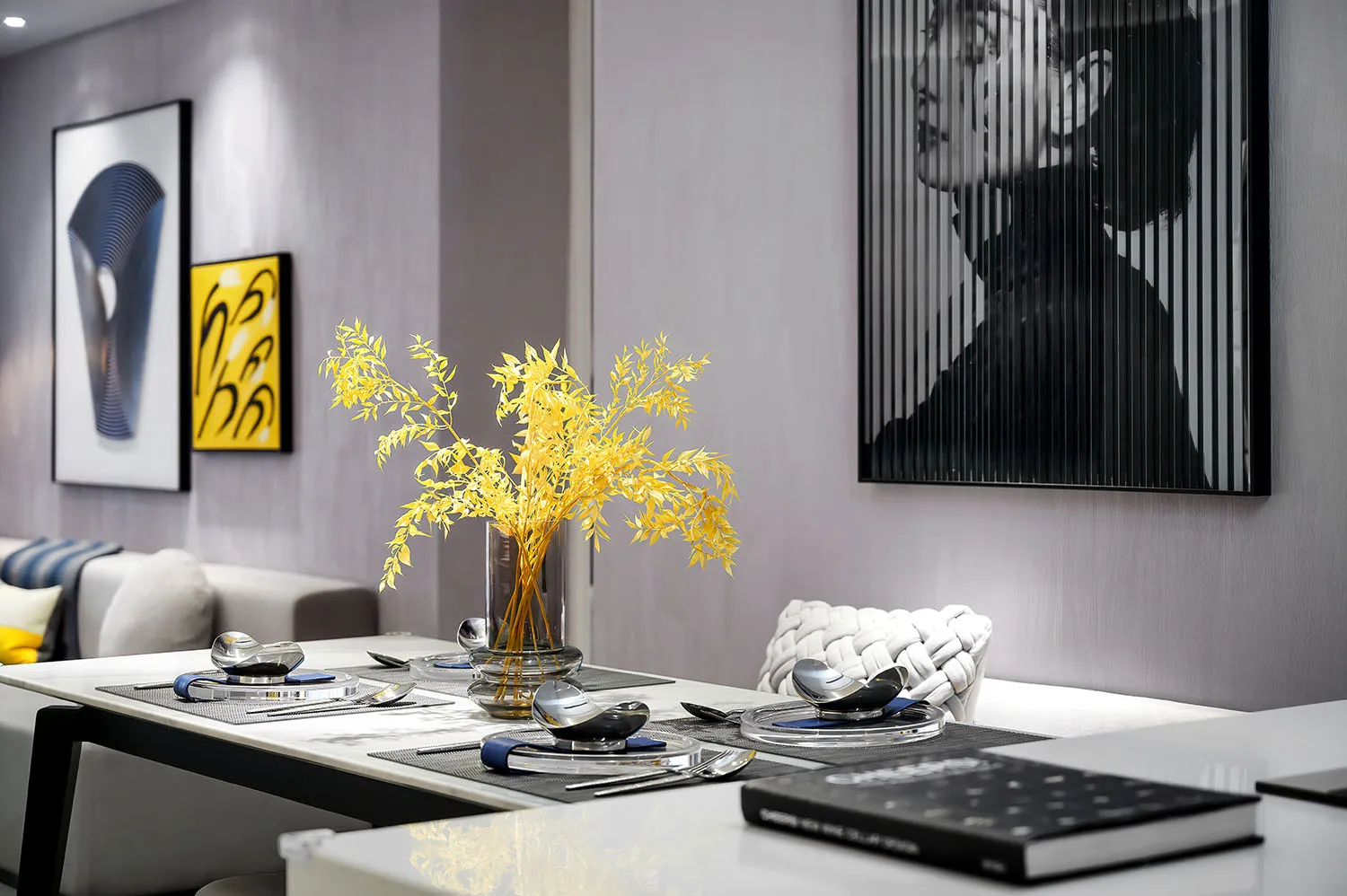Modern dining room with glass table, golden flowers in a vase, and sleek black and white design.