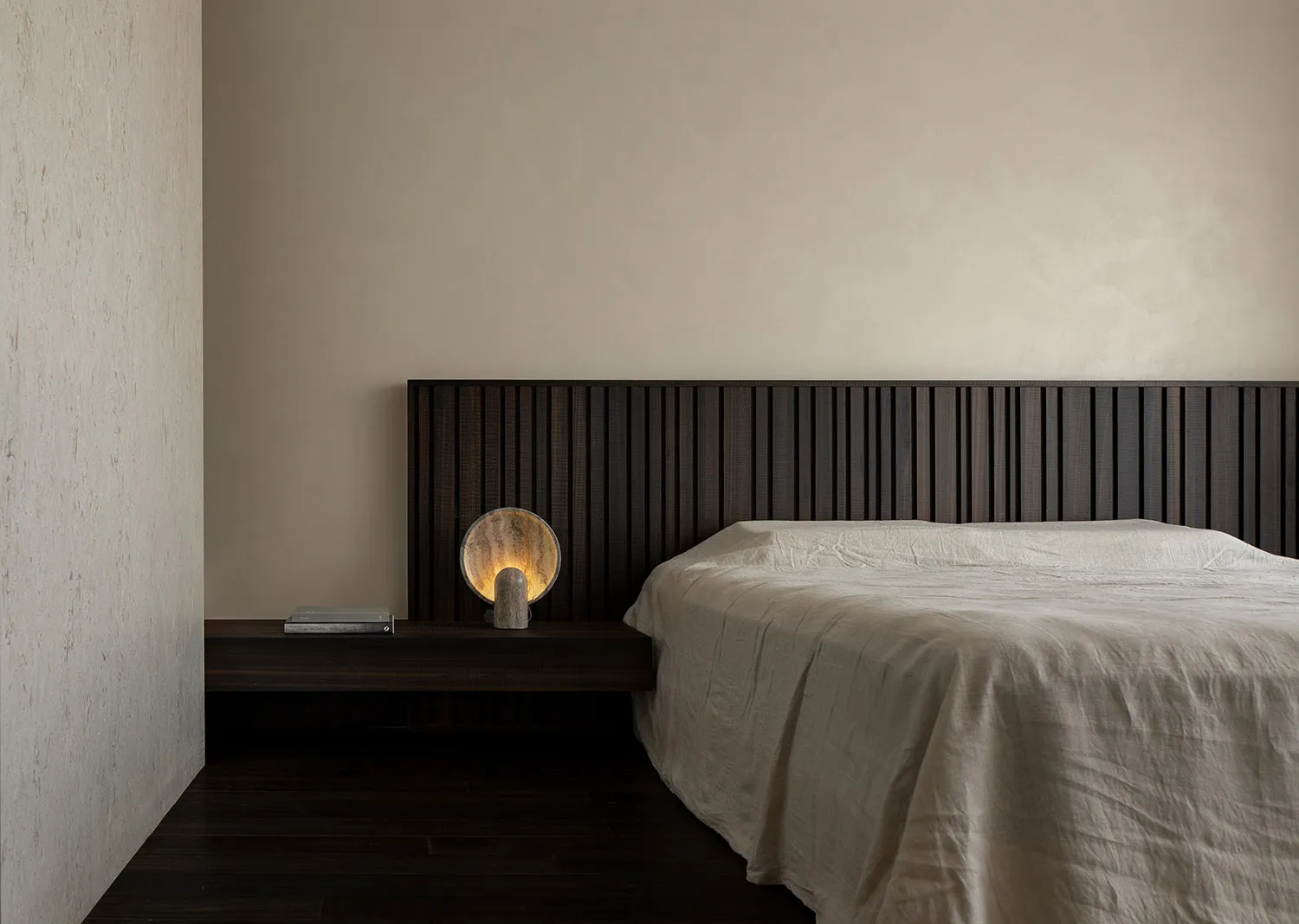 A minimalist bedroom with a wooden headboard and a light-colored bedspread.