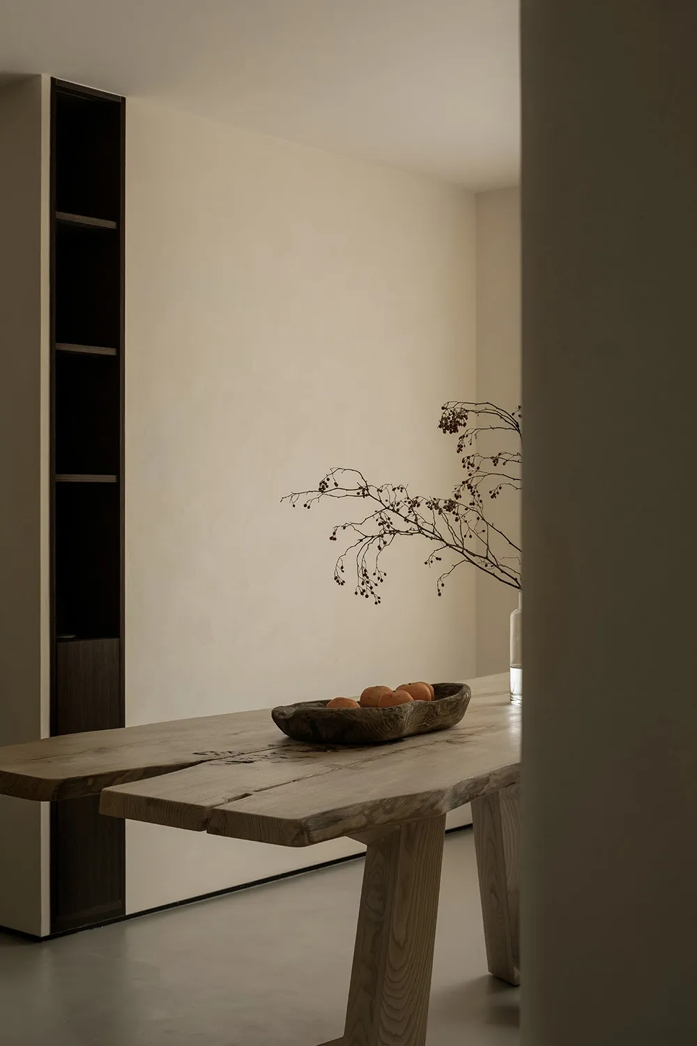 A minimalist interior design featuring a wooden table with fruits and a branch with berries.