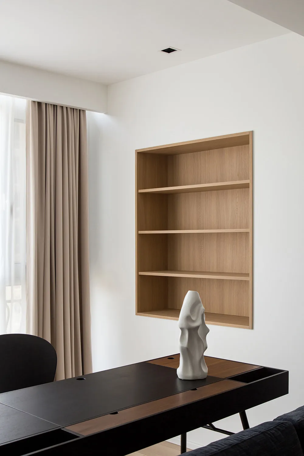 A minimalist living room featuring a wooden shelving unit with a white ceramic sculpture on a black and brown wooden table.