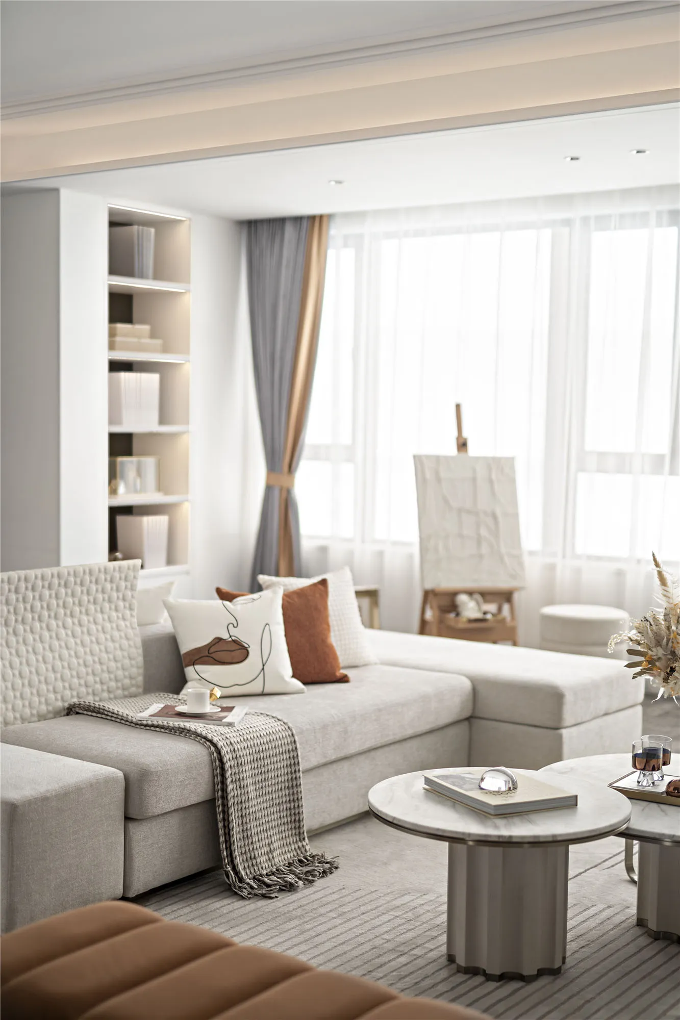 A modern living room with furniture arranged around a round marble coffee table, featuring neutral fabrics and minimalistic d