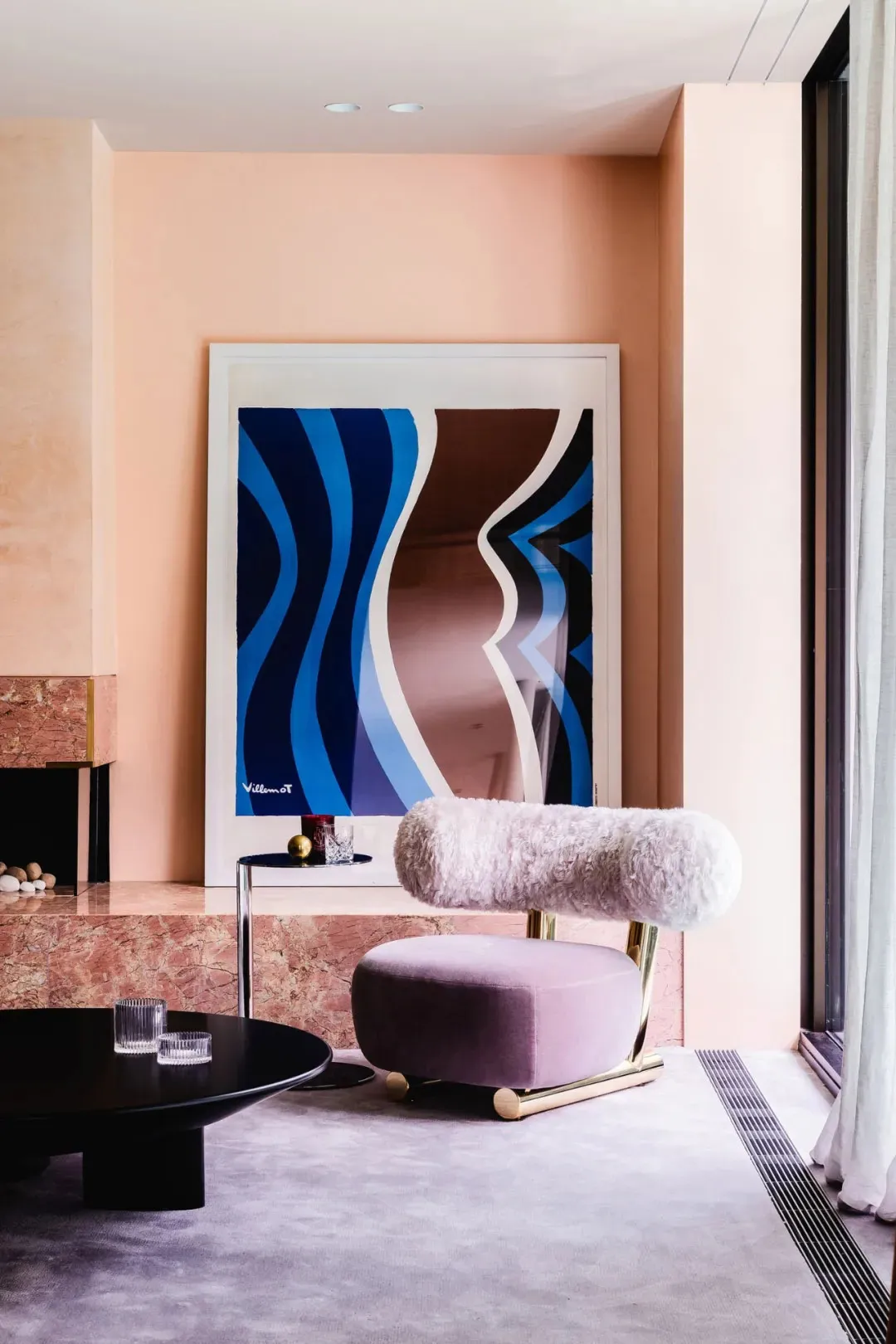 A modern living room with a marble fireplace, plush armchair, and abstract art hanging on the wall