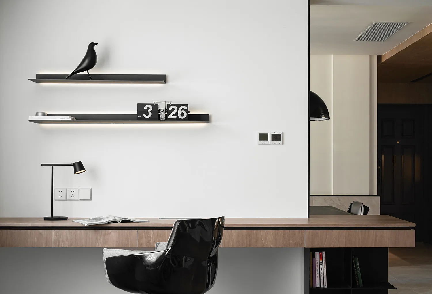 A minimalist workspace with wooden shelves, a black chair, and a desk lamp.
