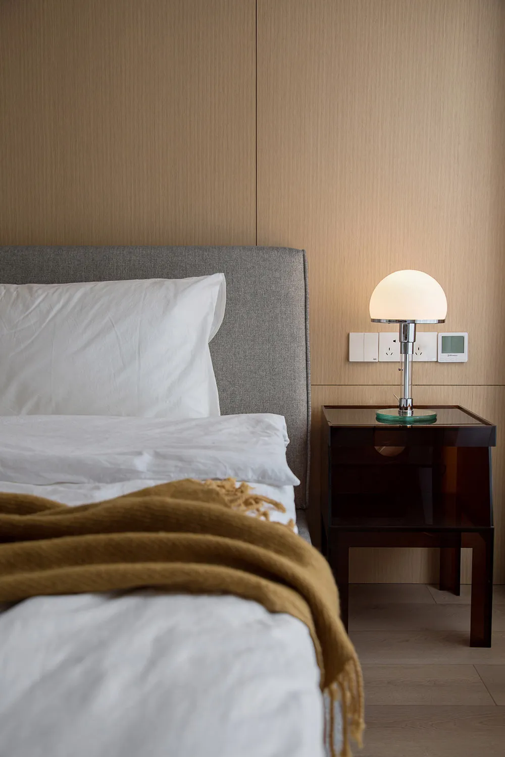 Bedroom featuring minimalist design with a grey headboard, white linens, and a mustard yellow throw blanket.