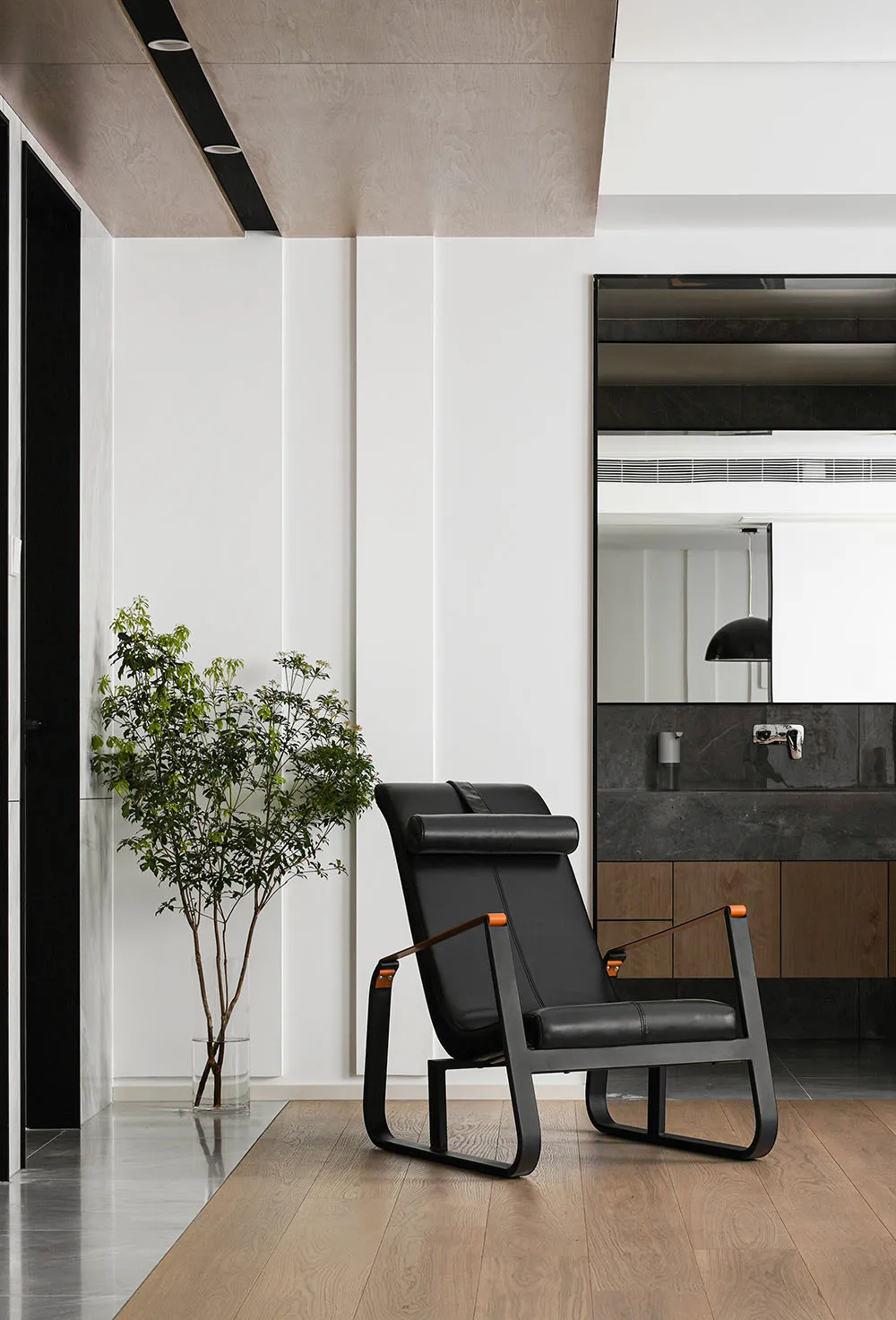 Minimalist design living room featuring a black leather chair, wooden flooring, and a potted plant.