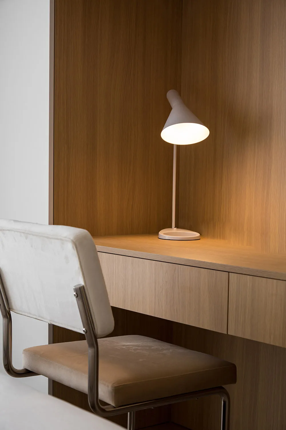 A minimalist office desk space featuring a wooden chair and table lamp.