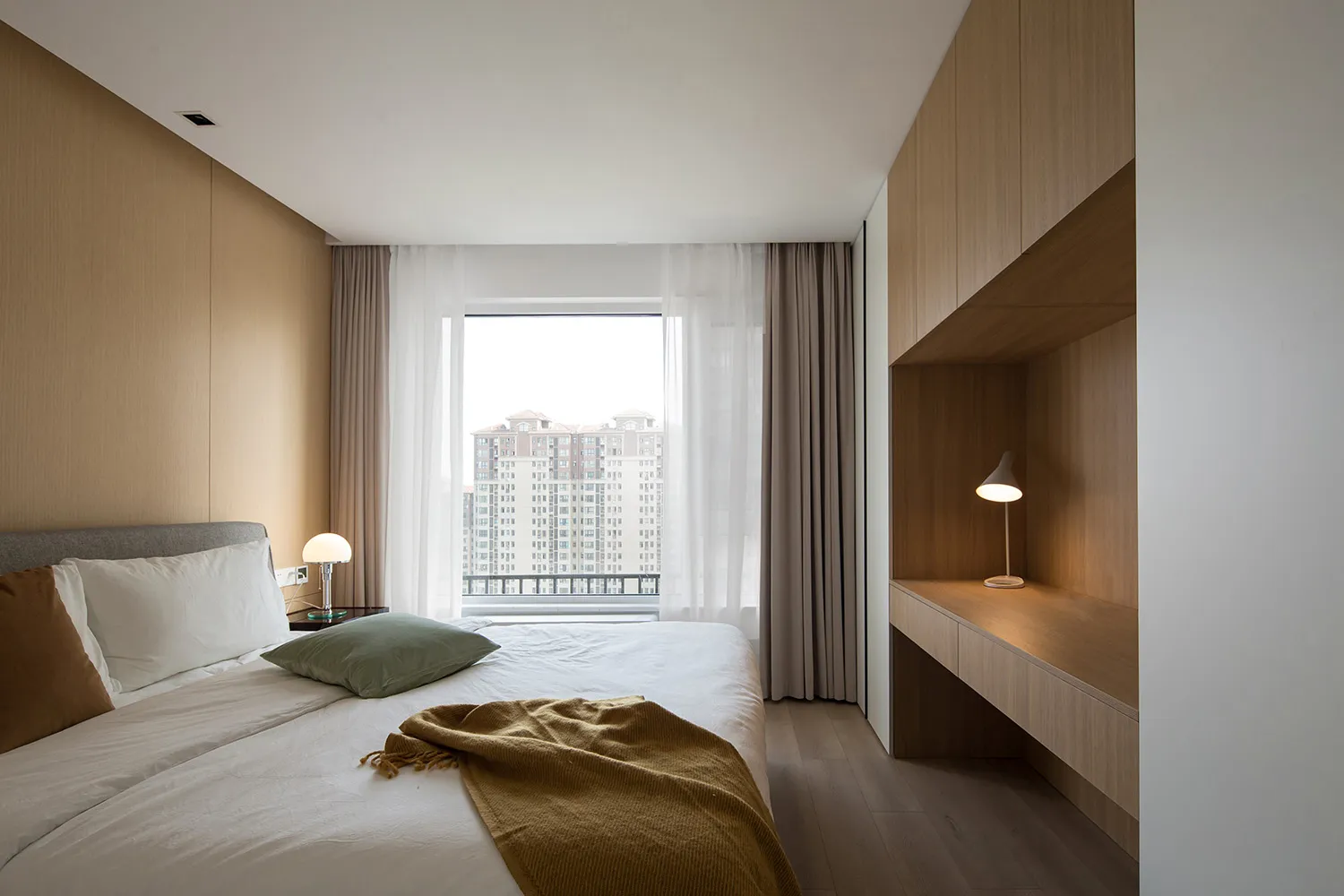 A modern minimalist bedroom with white curtains and wooden furnishings.