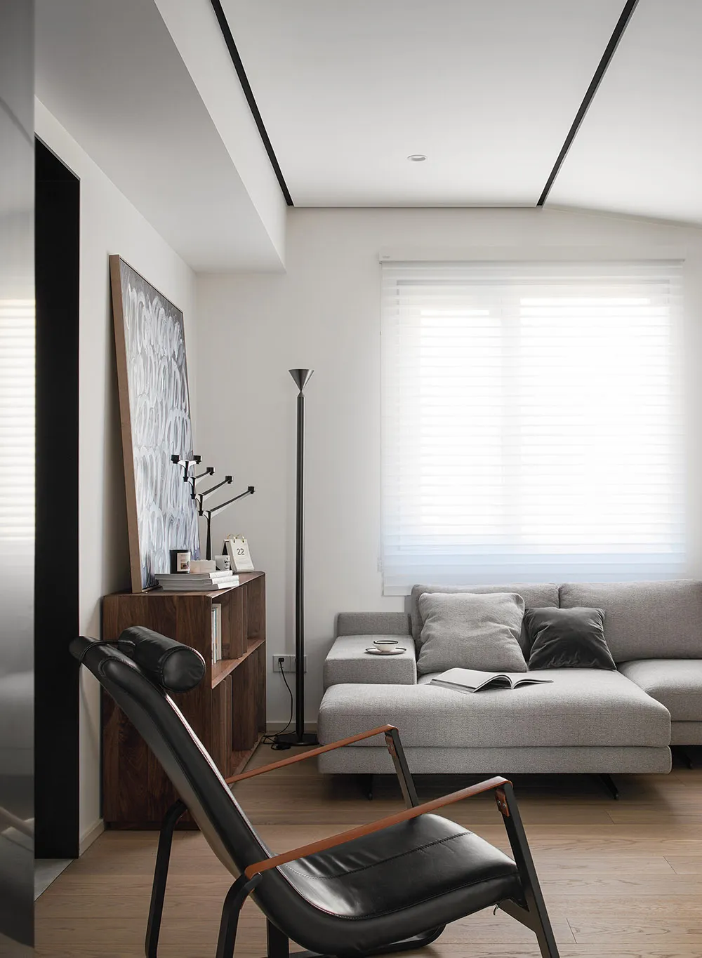Minimalist living room with a gray sectional sofa, black leather chair, and wood floor.