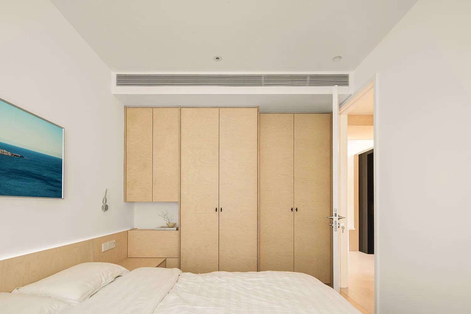 A minimalist bedroom featuring wood cabinets and a bed with white sheets and pillows.