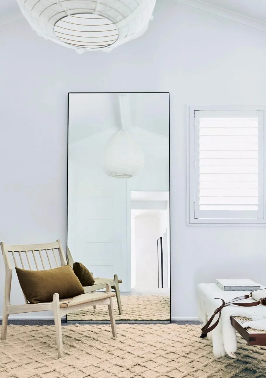 A minimalist living room with white walls, wooden furniture, and a large mirror.